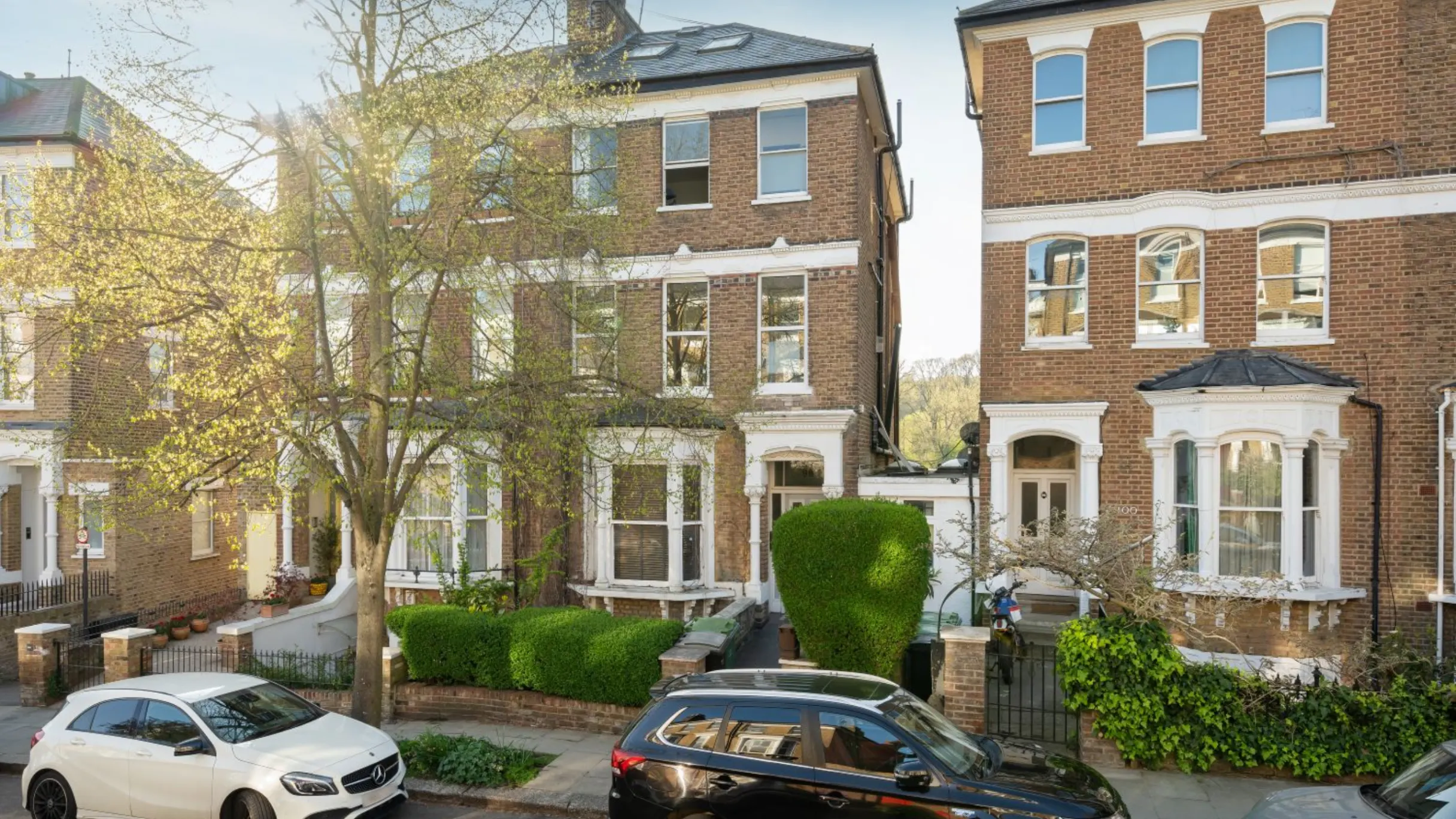 Exterior of two Victorian three story properties with bushes and a tree outside