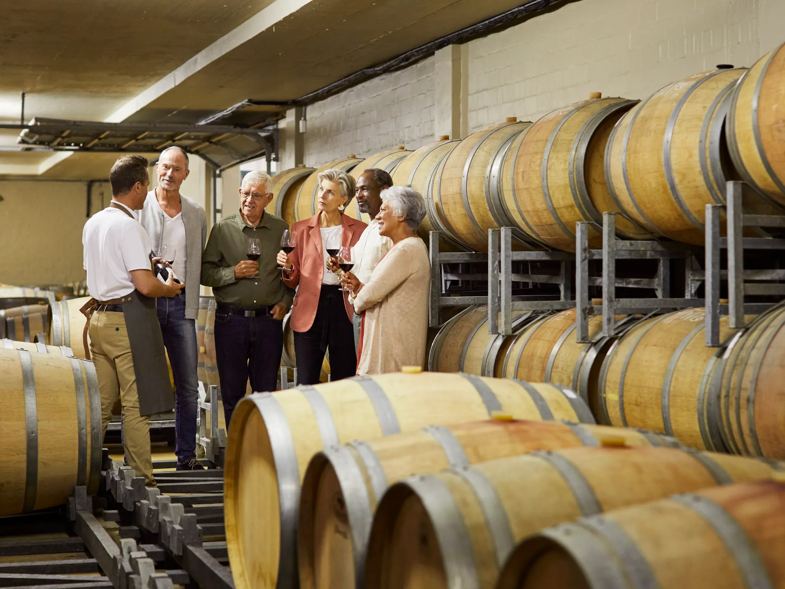 Sommelier talking to a group of people, surrounded by wine casks. 