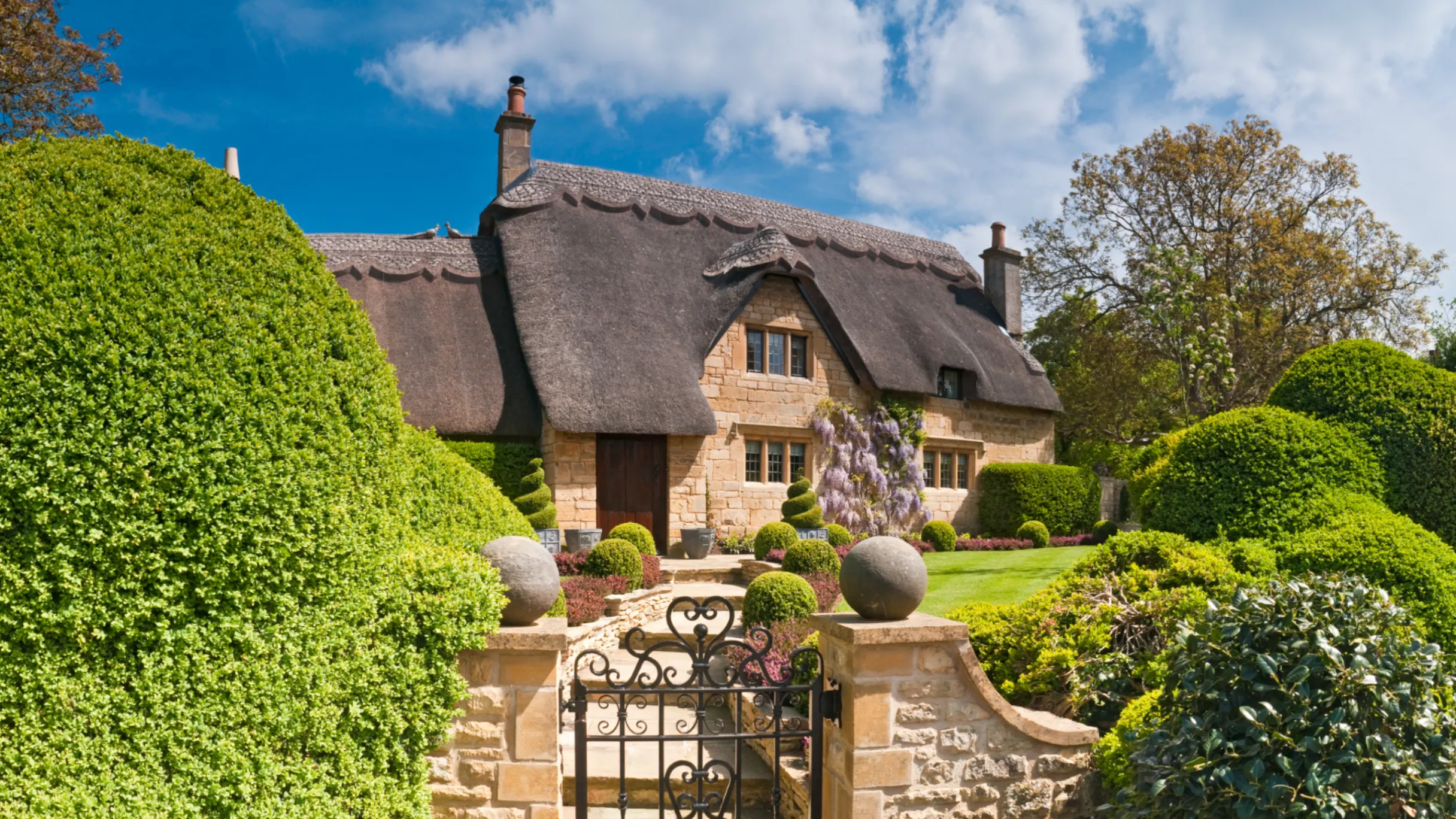 idyllic country cottage thatched roof pretty summer gardens Cotswolds UK