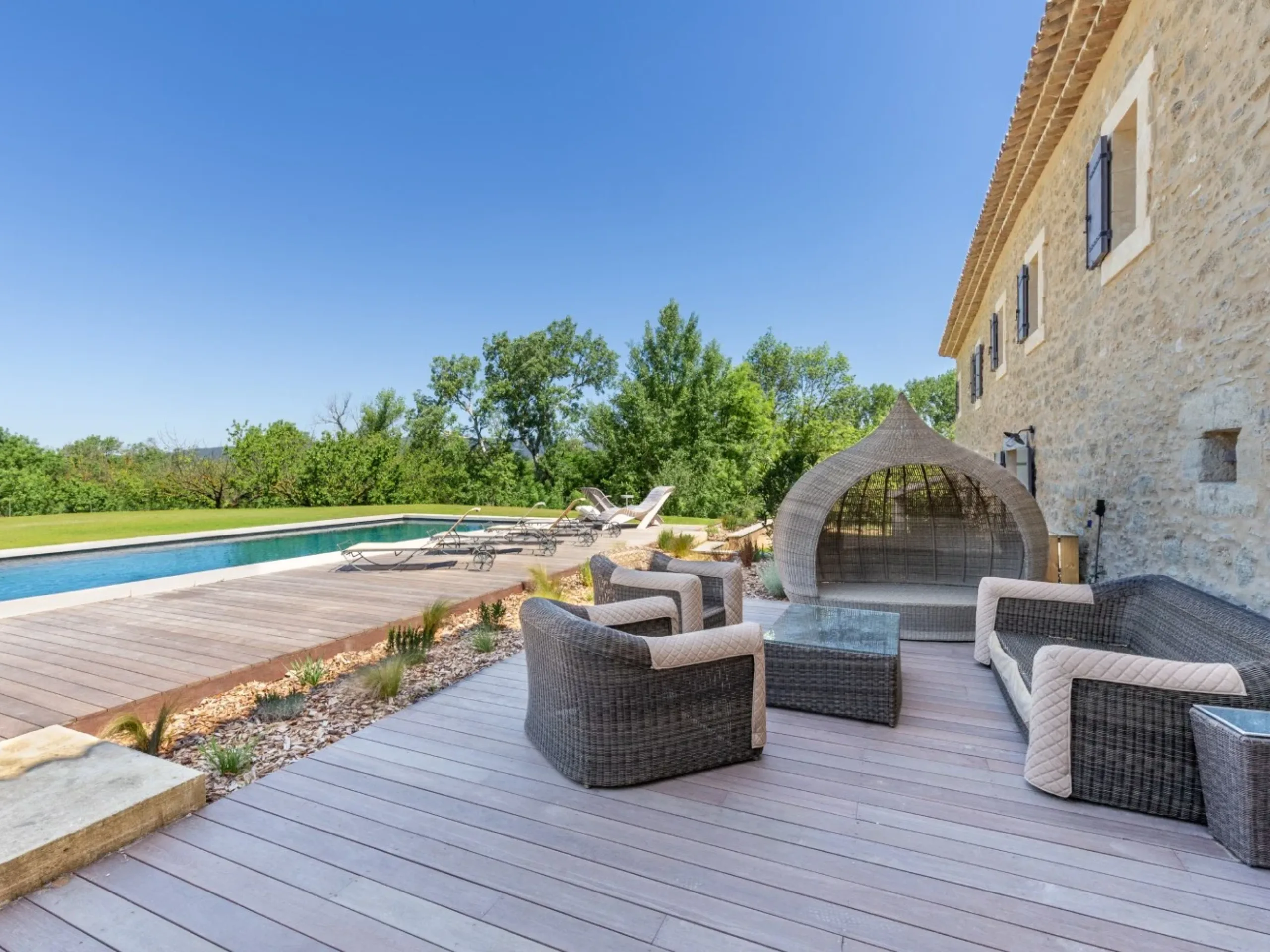 Poolside terrace with woven chairs and trees in the background