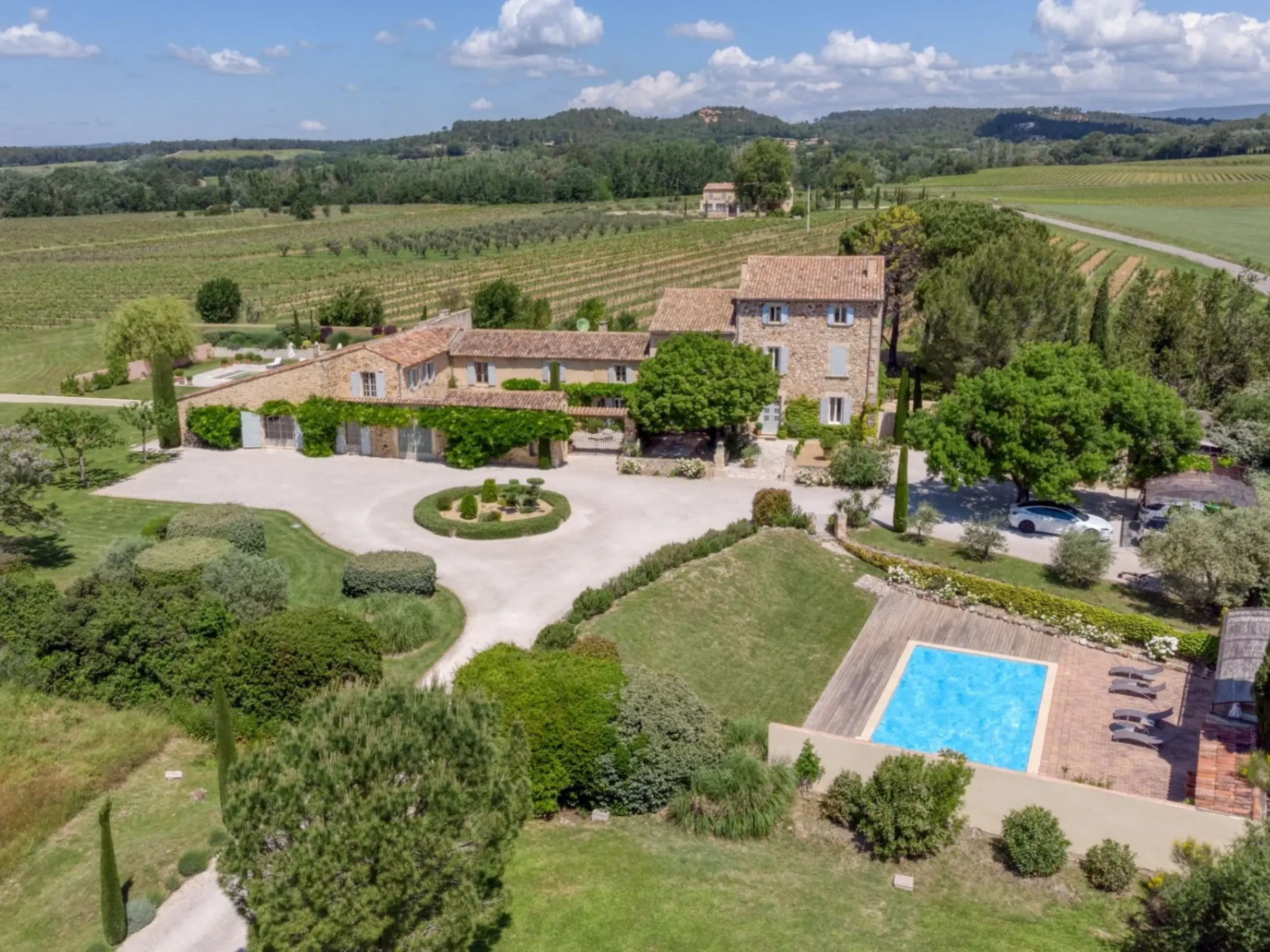 Ariel shot of a villa surrounded by fields, trees and with an outdoor swimming pool
