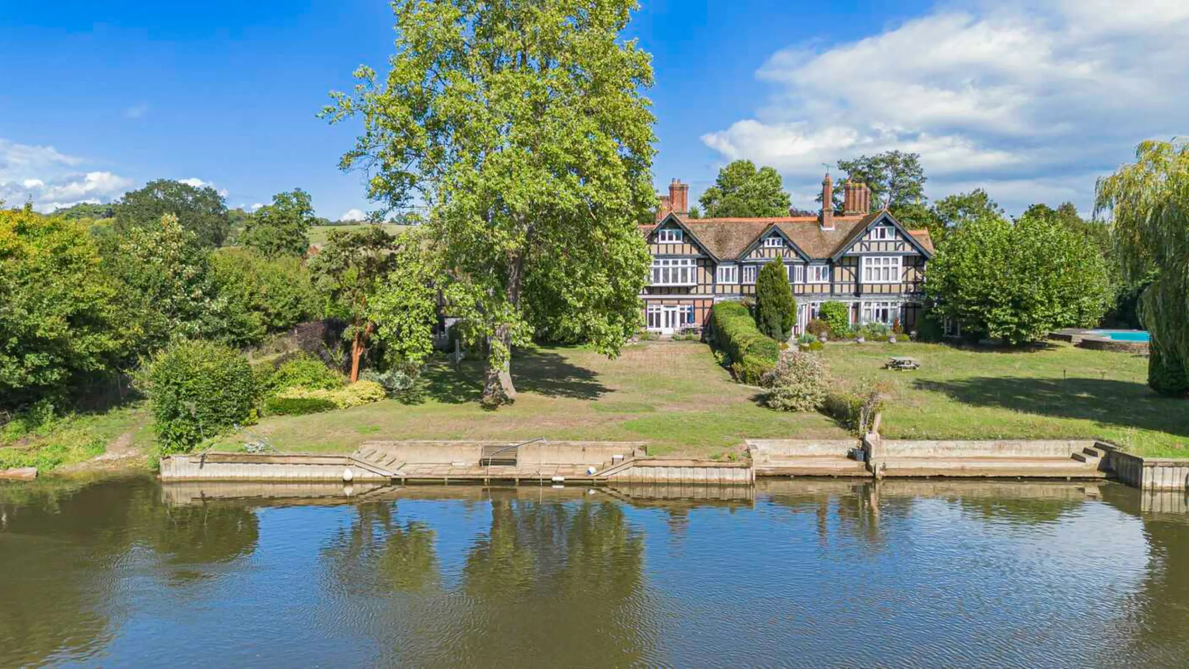 Exterior of a home surrounded by trees and with a large lawn leading down to a river