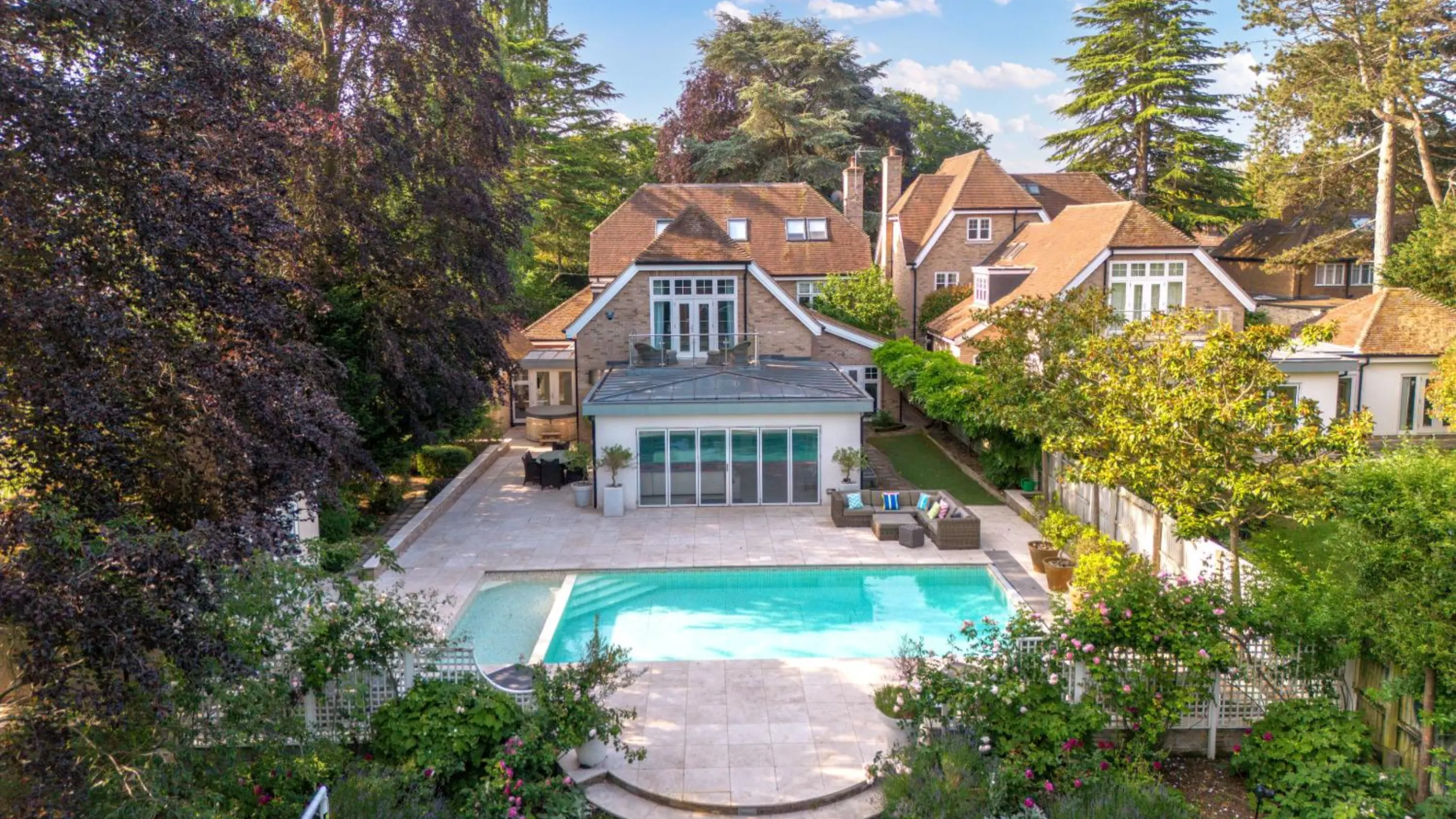 Back garden with a swimming pool in it and the exterior of a house surrounded by trees