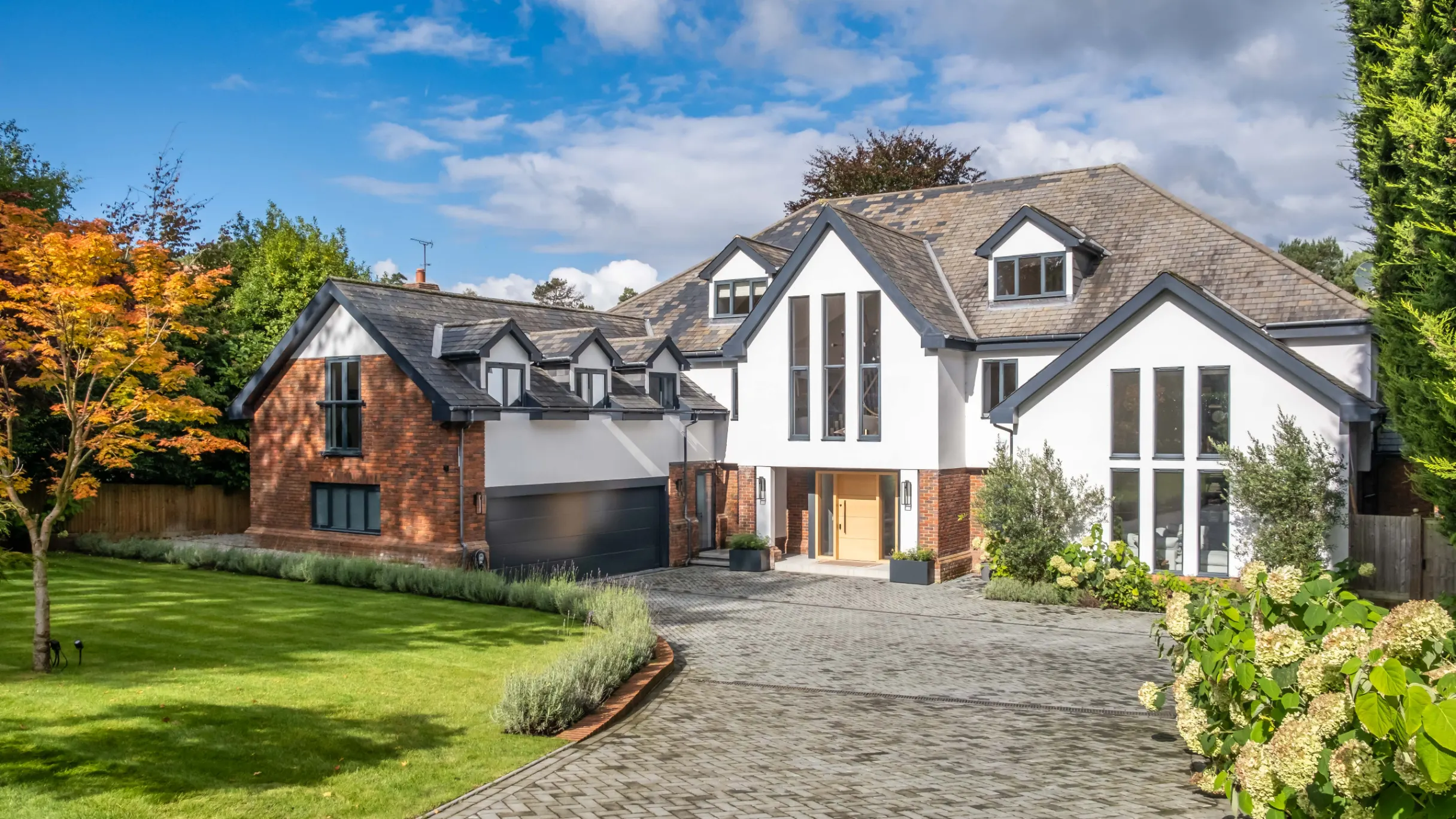 Large house with white and redbrick exterior and large driveway and front garden