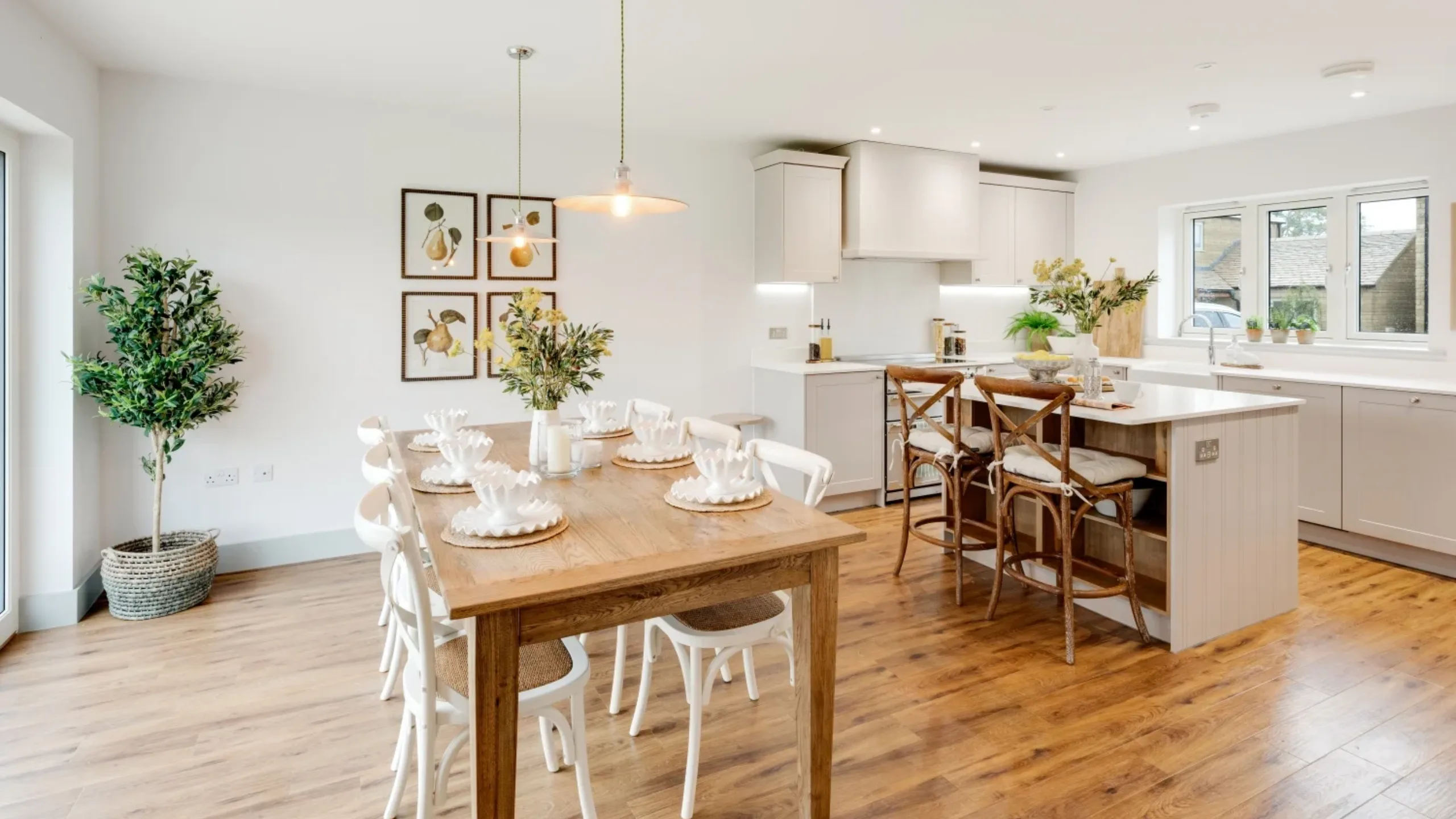 Living room with brown dining table and white chairs and white kitchen island and stools and white cabinetry with light brown wooden floors