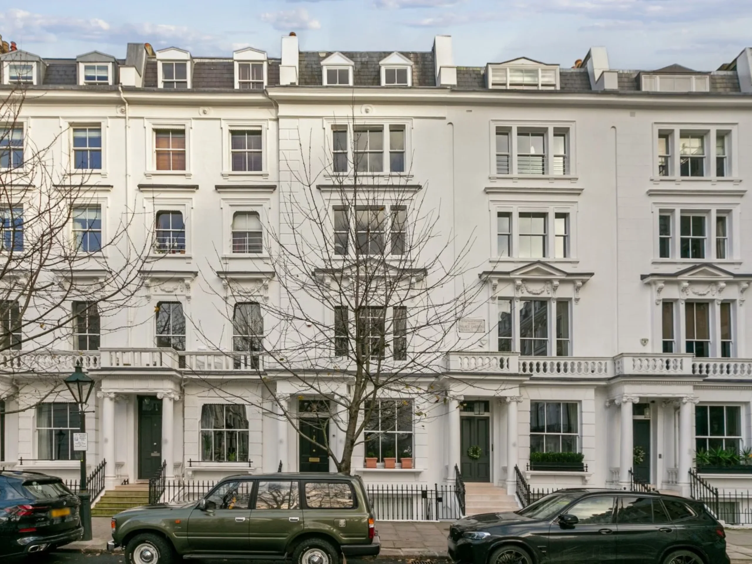 Row of white period townhouses with sparse trees and cars in front