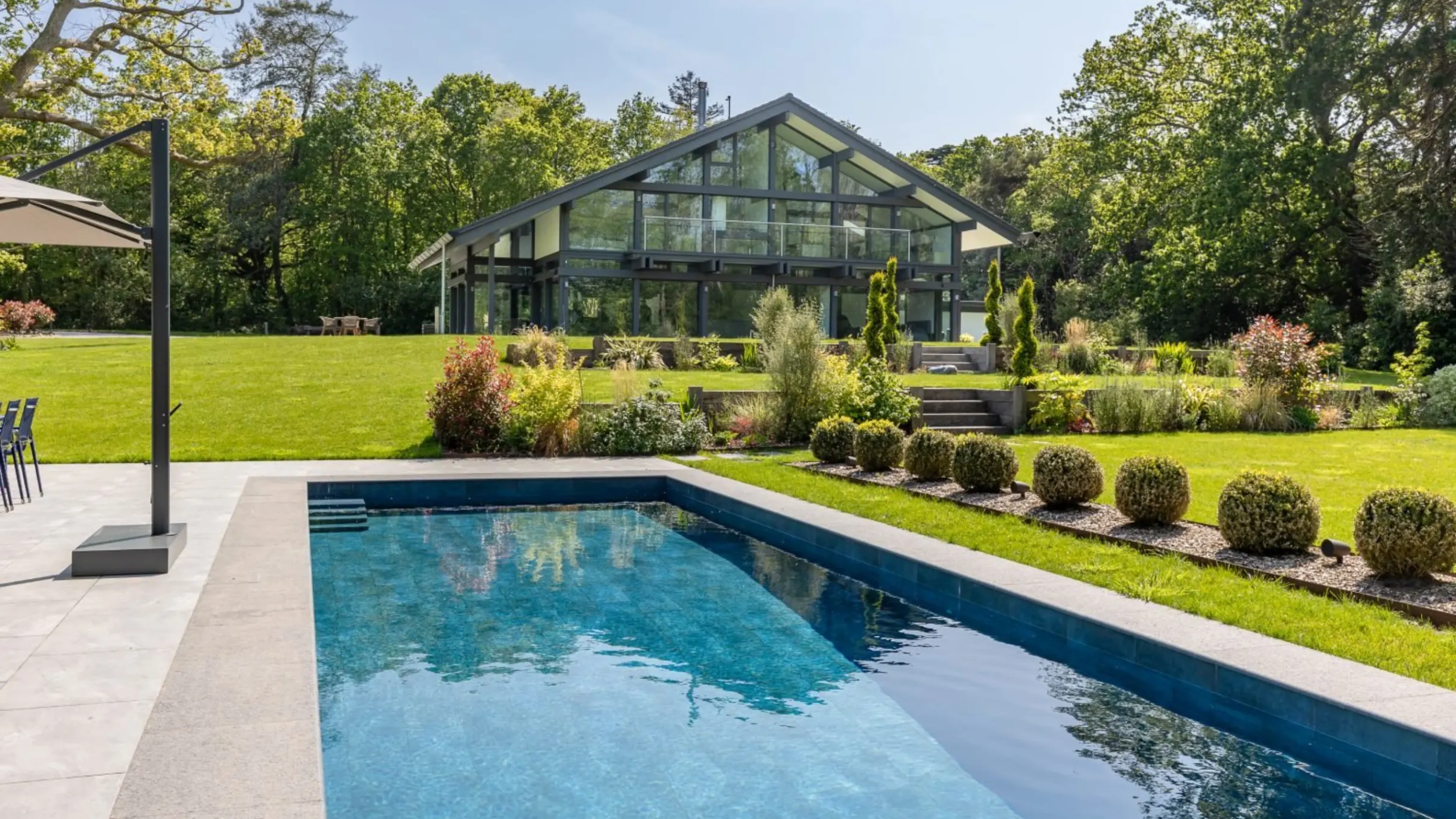 Garden with green lawn, swimming pool and the exterior of a large multiple windowed house