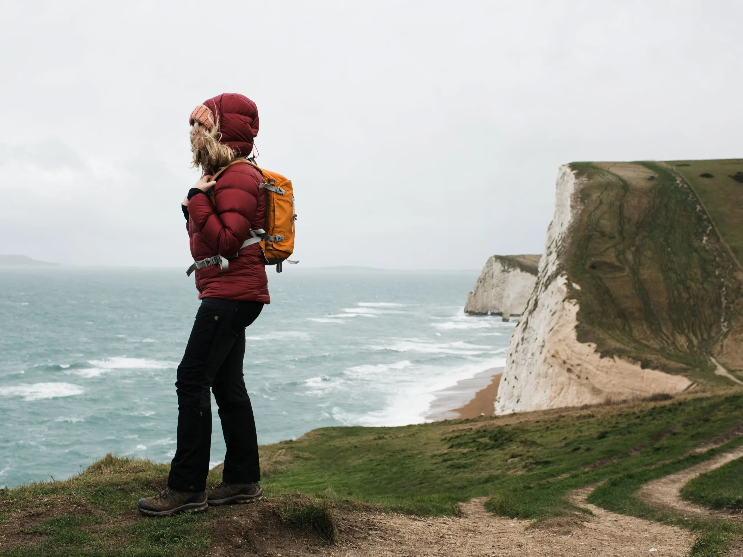 A woman in a red coat standing on a cliff edge with the sea in the background