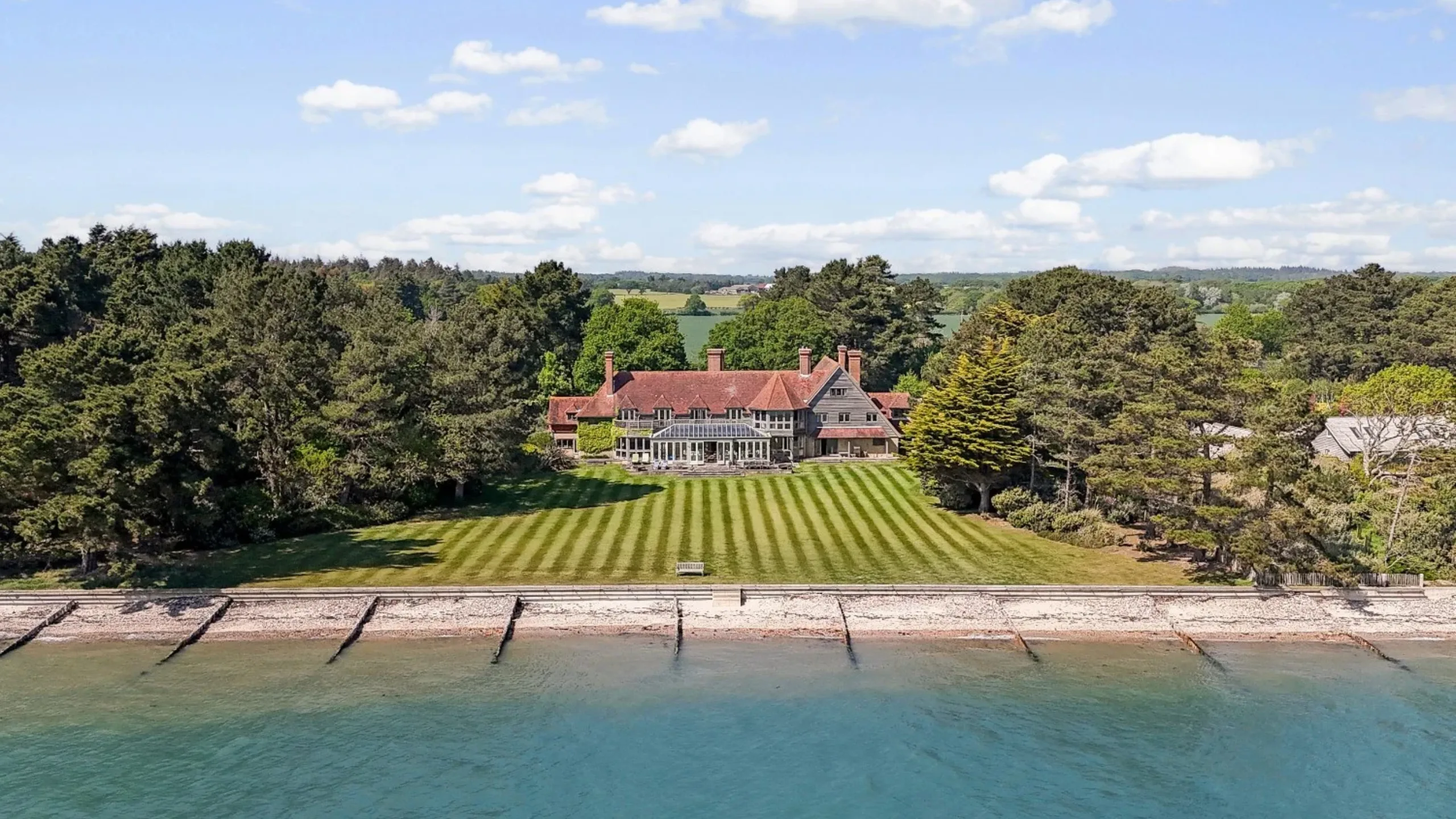 Ariel view of large house surrounded by field and trees opening on to sea