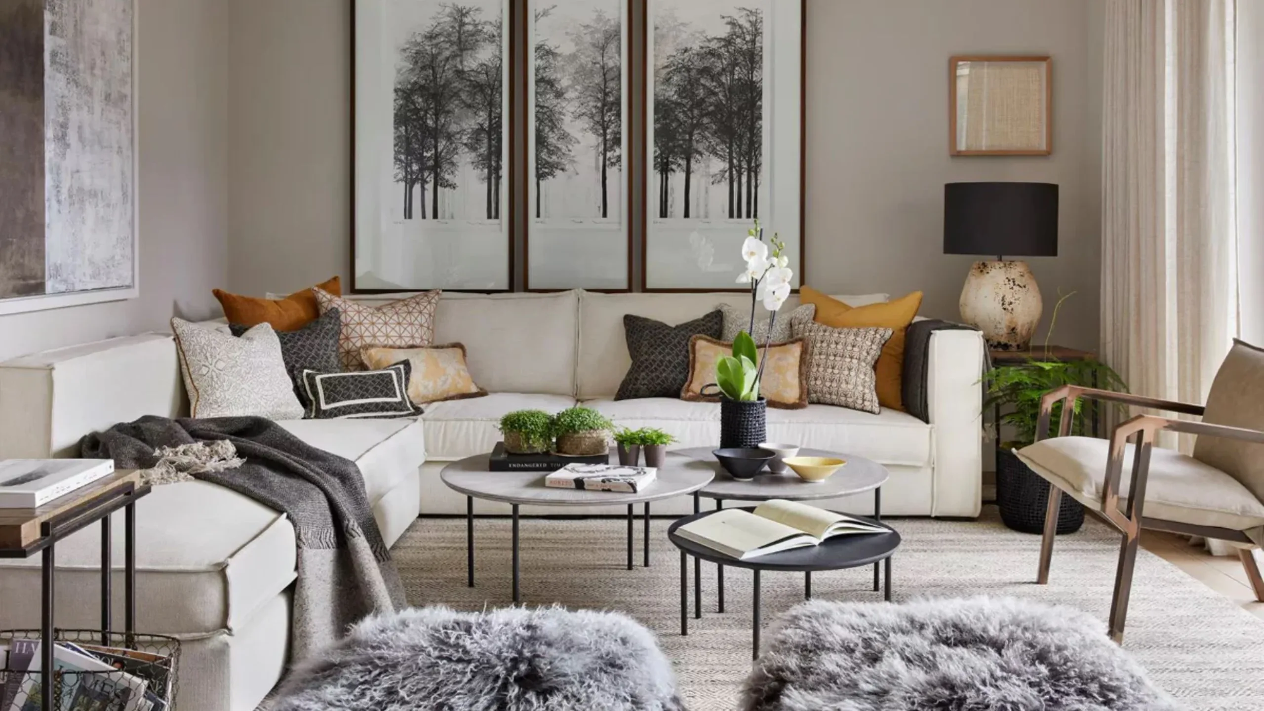 High end living room with cream sofa with multiple cushions, grey coffee tables and photographs of trees on the wall
