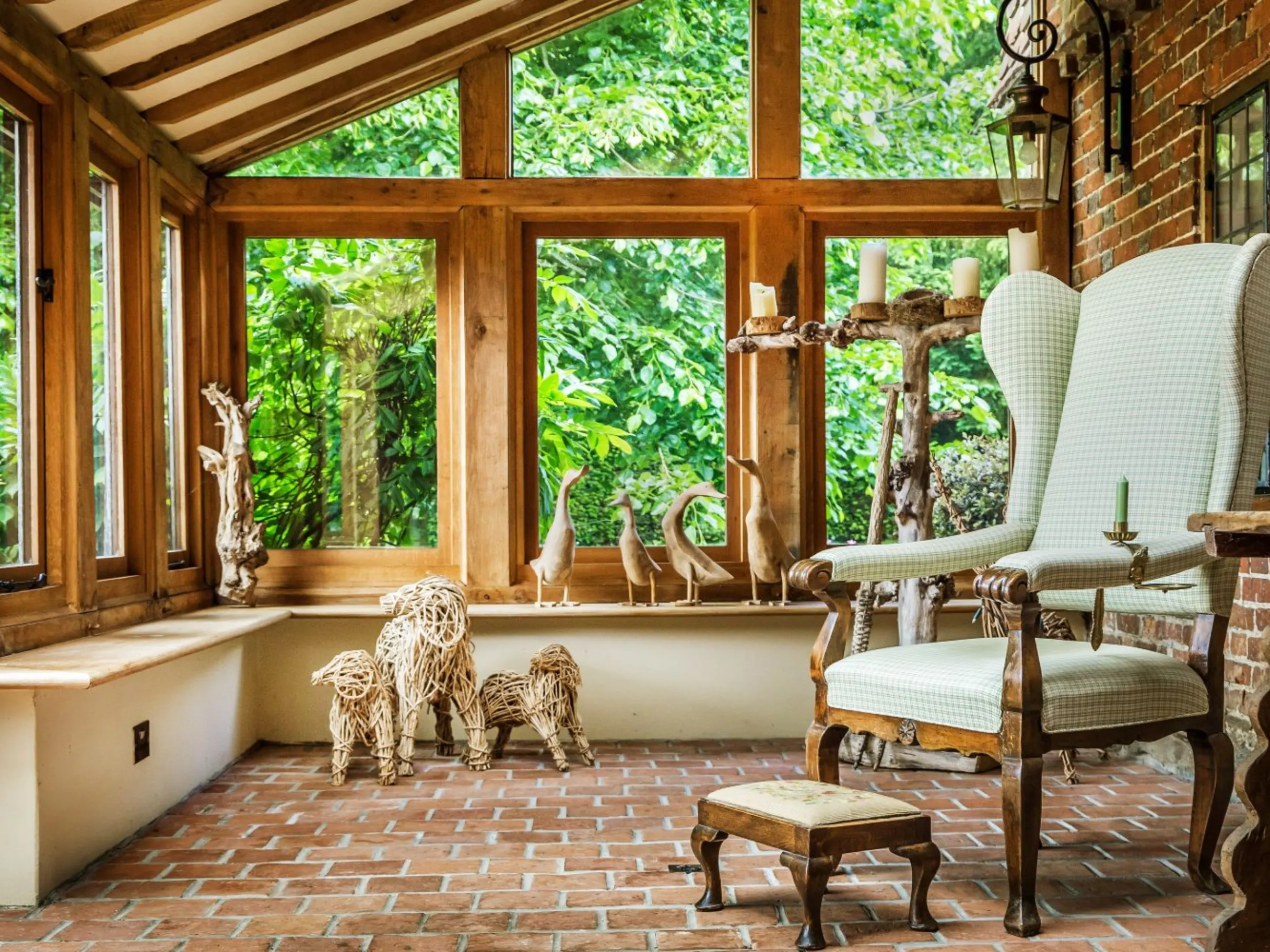 Conservatory with brick flooring, wooden window panes, a large chair and stool and ornamental sculptures