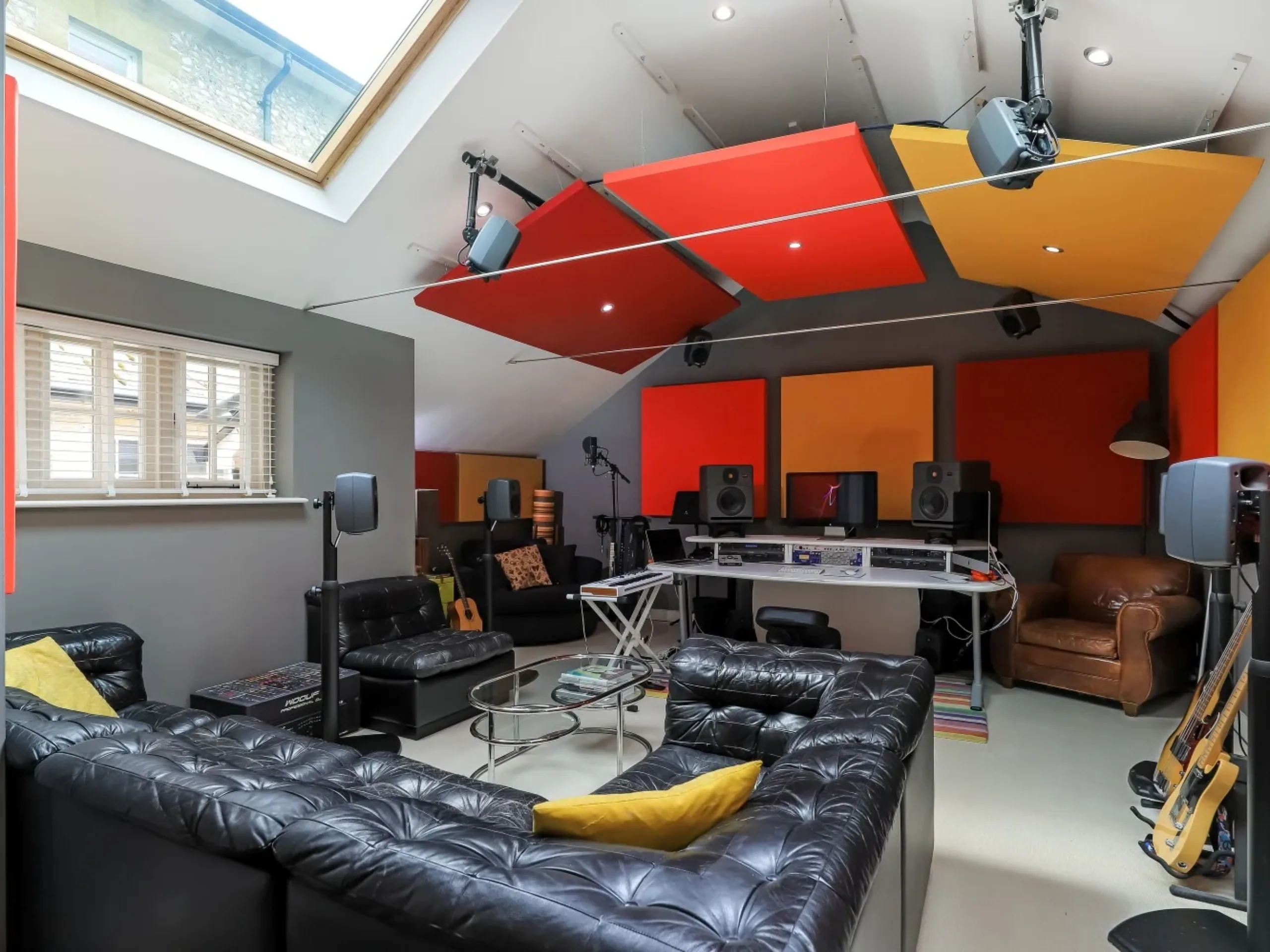 Home recording studio with black leather sofa, desk, speakers and red and orange screens
