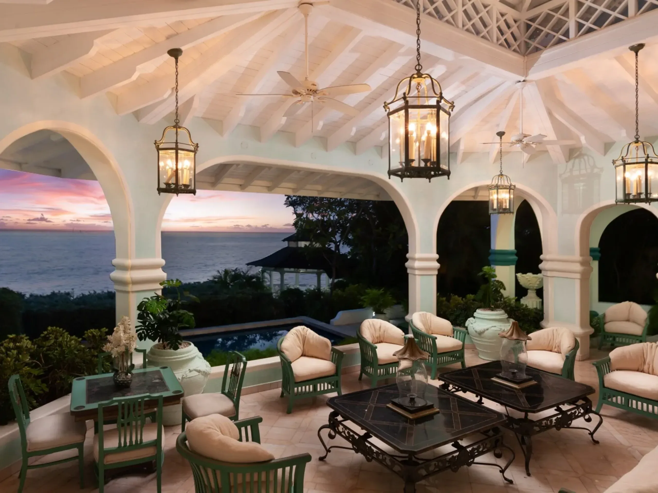 outdoor covered terrace at night with green chairs and black coffee table with lanterns hanging from the ceiling