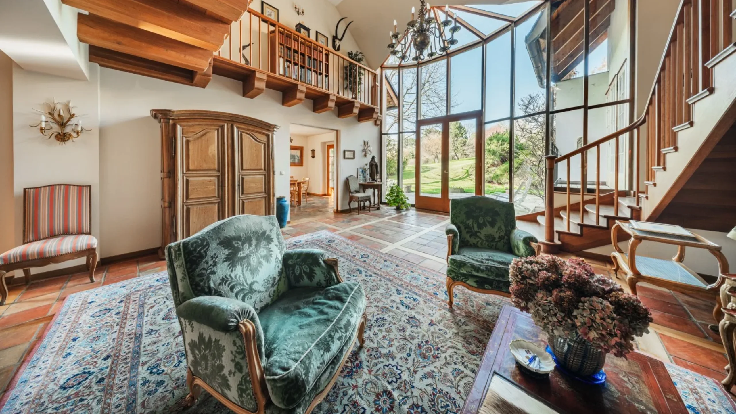 Living room with patterned rug and armchairs, with a wooden staircase and mezzanine and large floor to ceiling windows