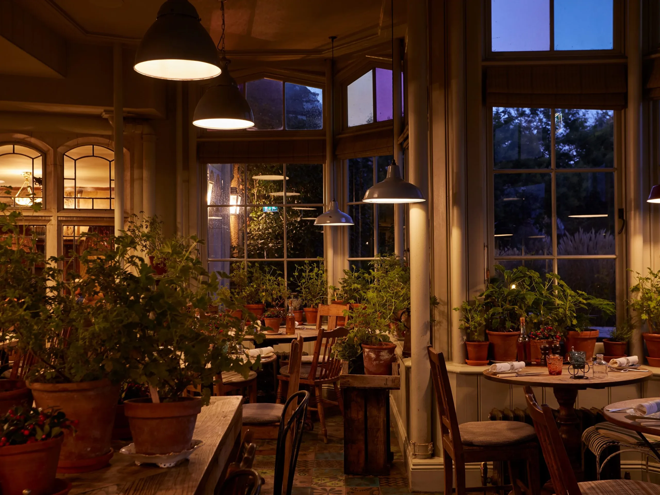 Restaurant in the evening with dining tables and chairs with plants on top of the table