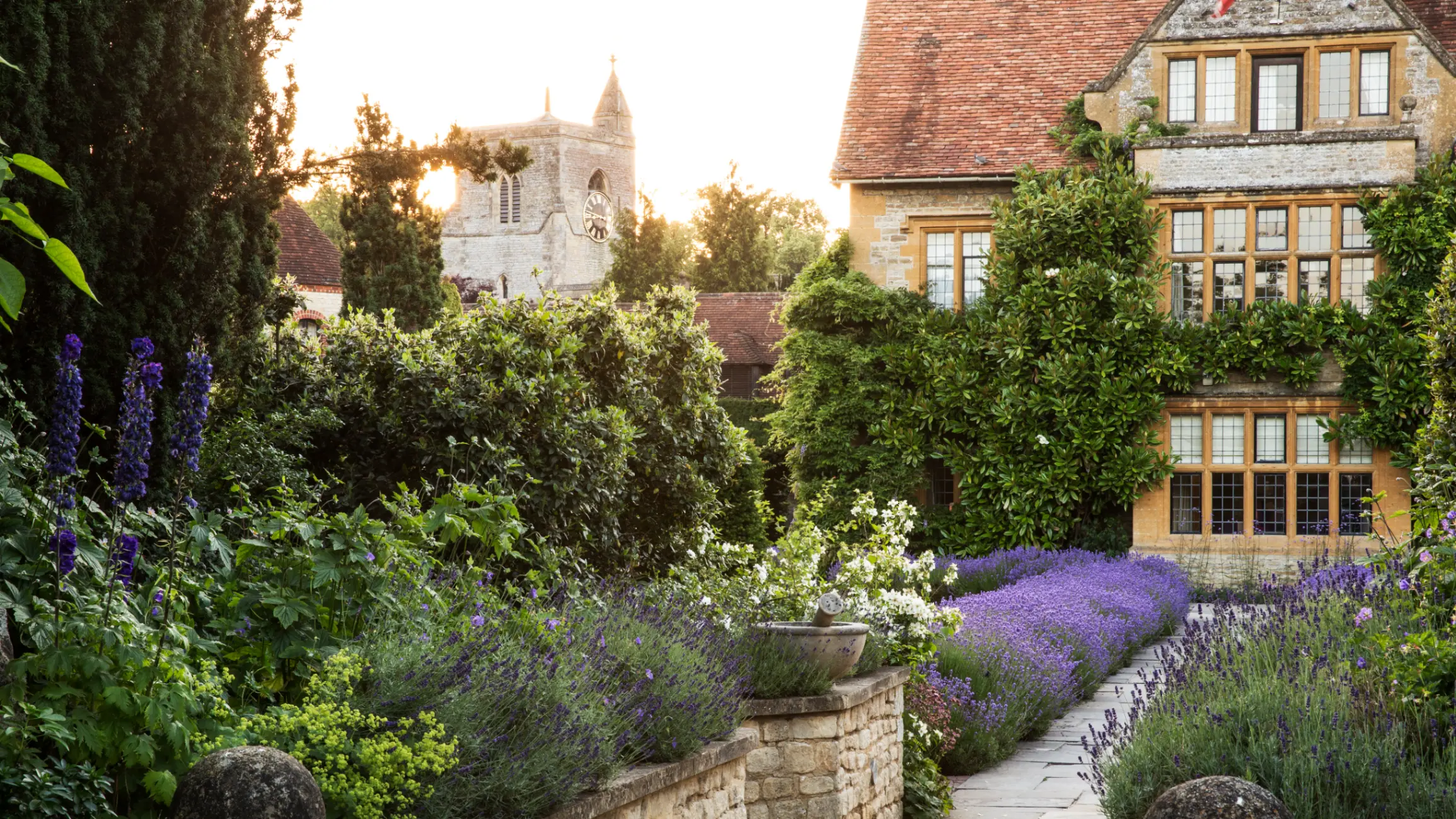 View of historic manor house from a walled garden with path and flowerbeds