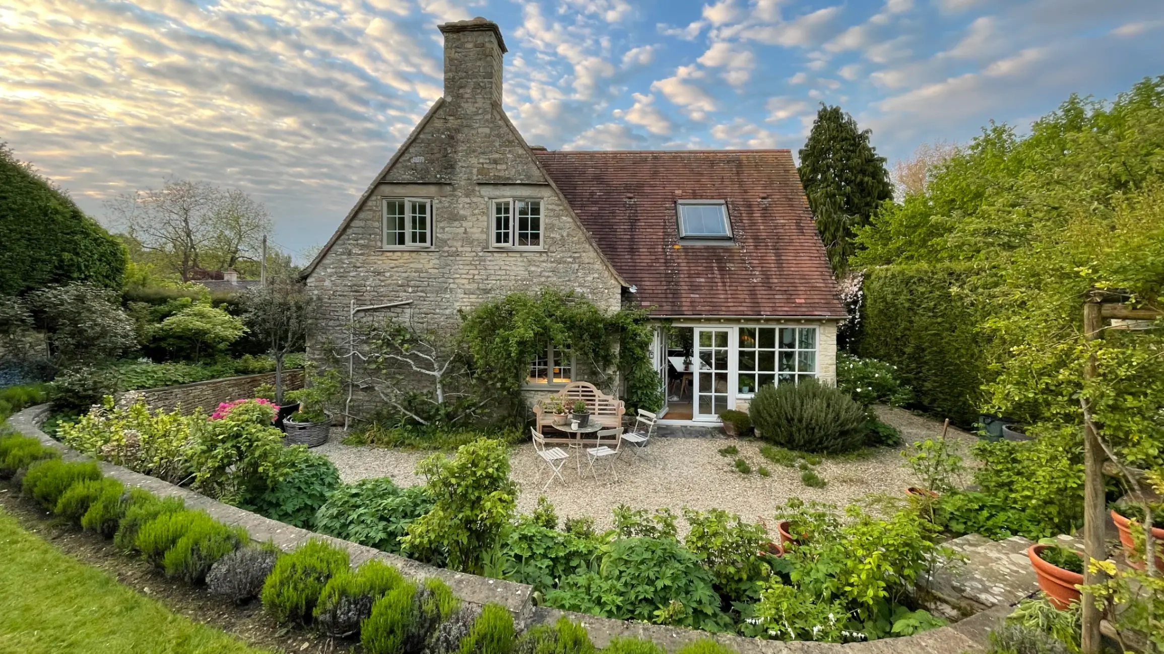 Exterior of period cottage with a gravel filled front garden surrounded by trees and bushes