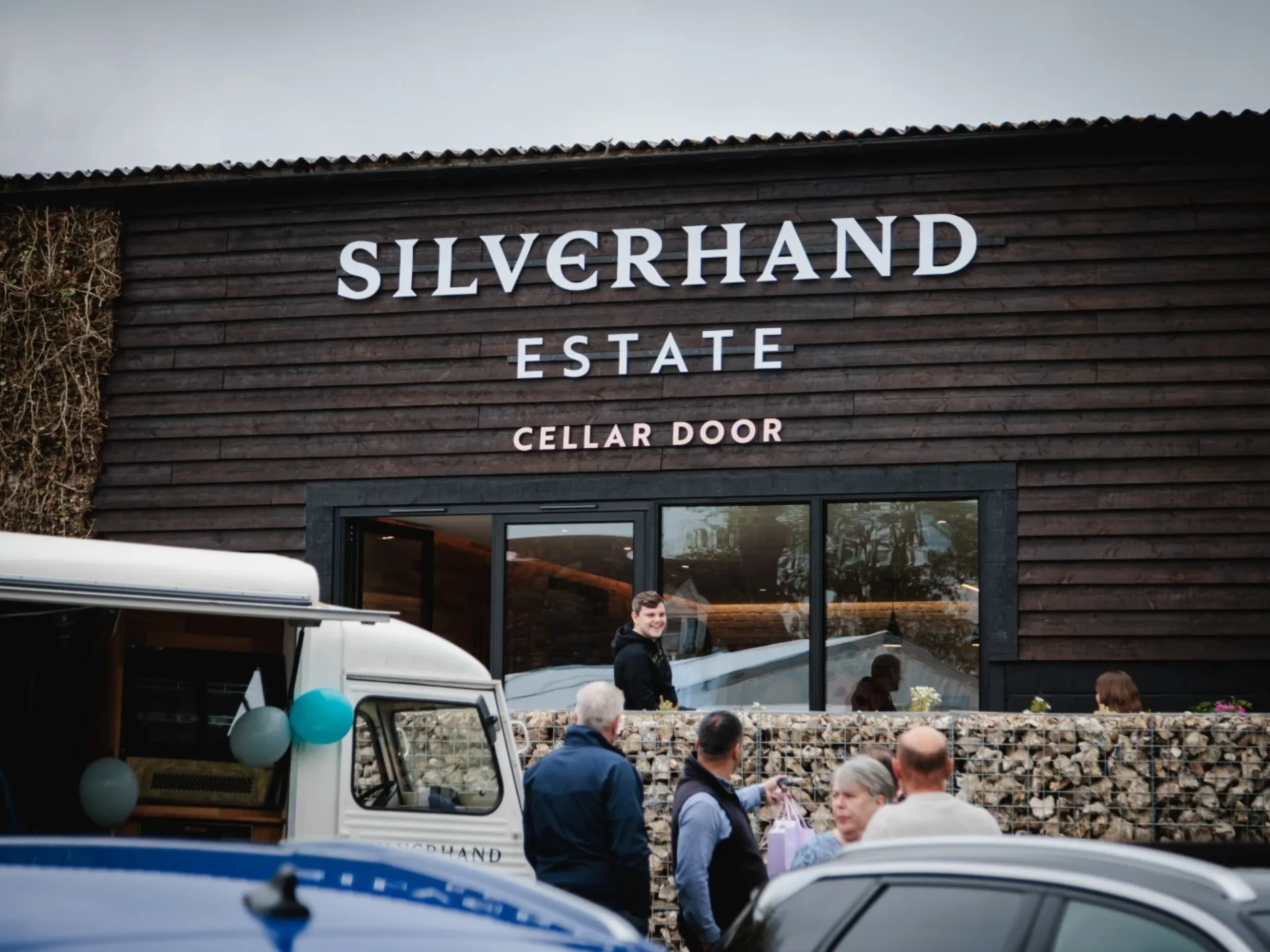 Shop with wooden brown exterior with the words Silverhand Estate Cellar Door on it, with people and cars standing outside of it