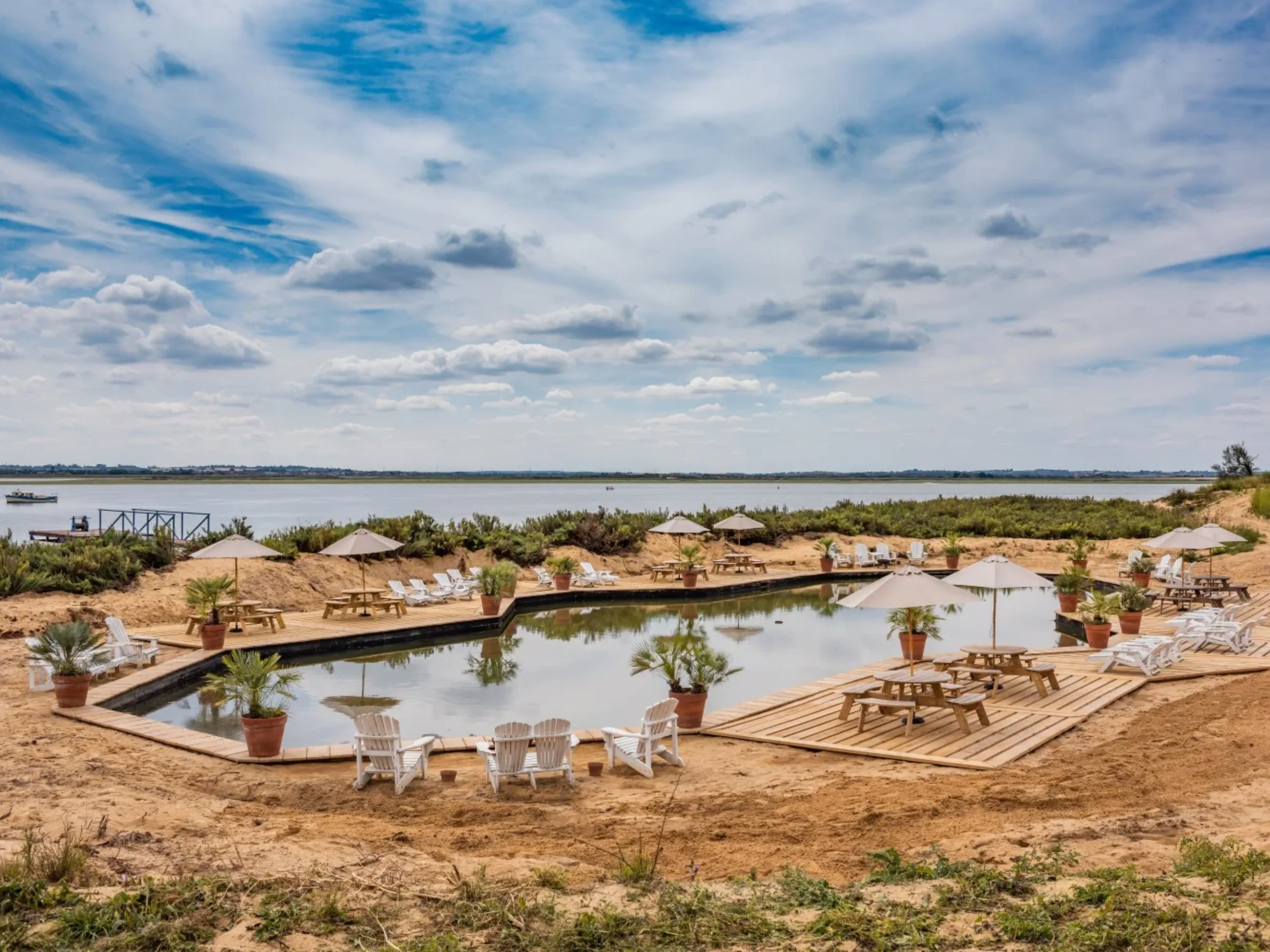 Natural pool surrounded by sand and plant pots with an estuary in the background