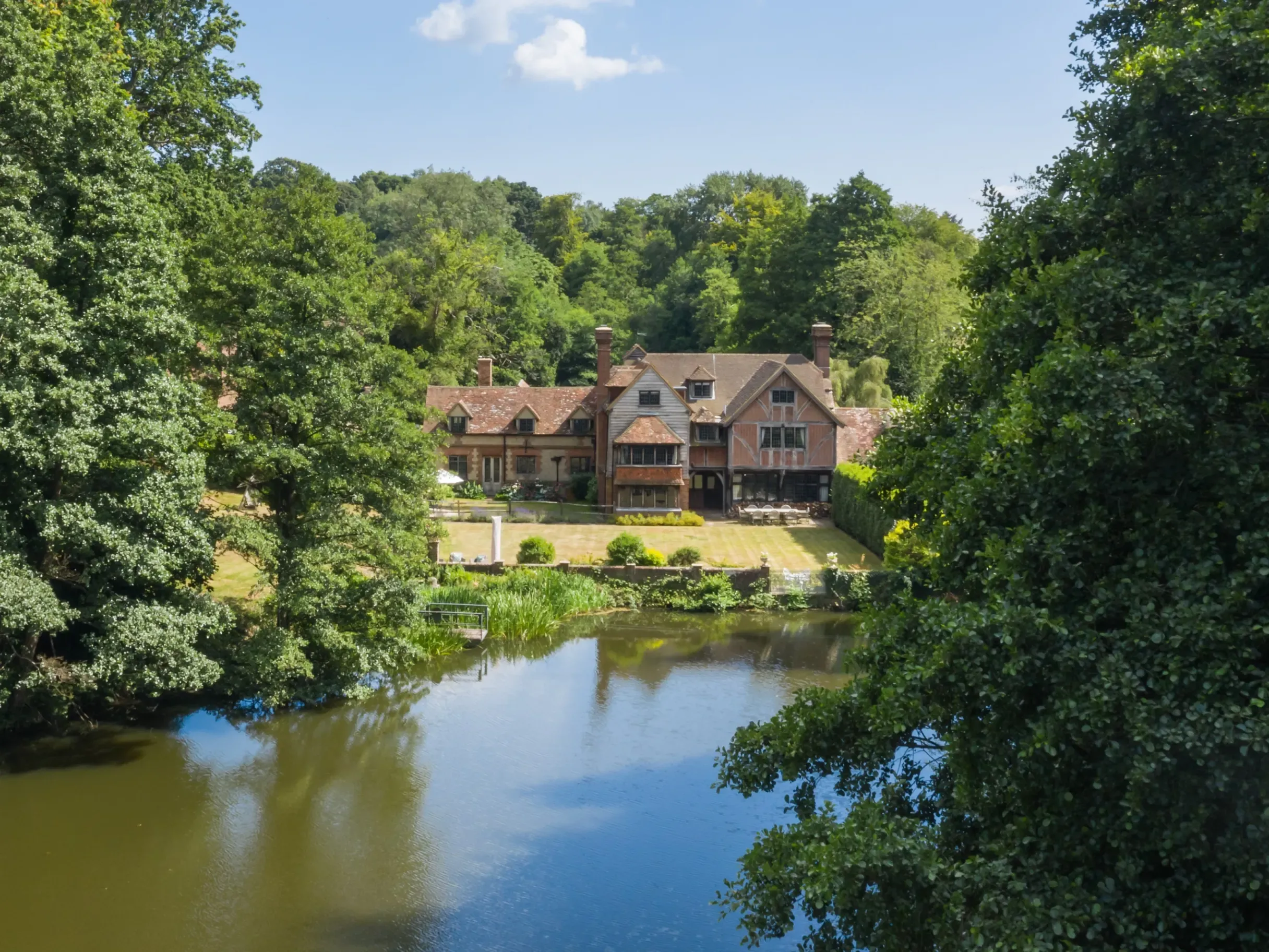 Exterior of large riverside country home surrounded by trees with a river in front of it
