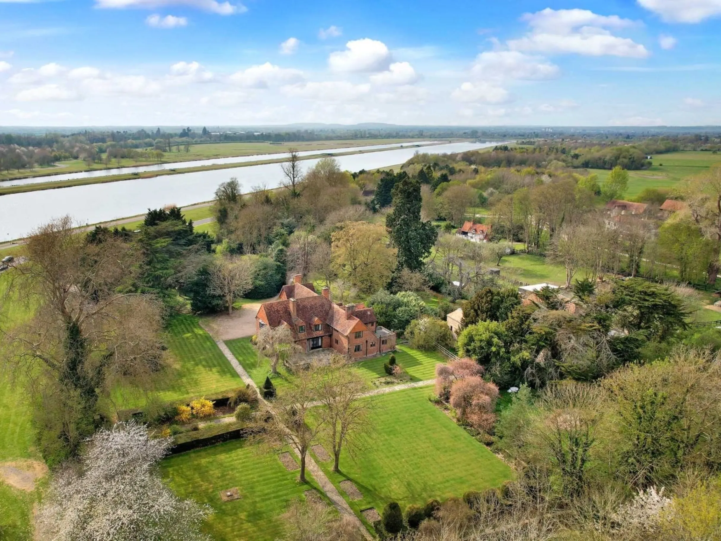Ariel shot of large period home surrounded by fields and trees with a river in the background