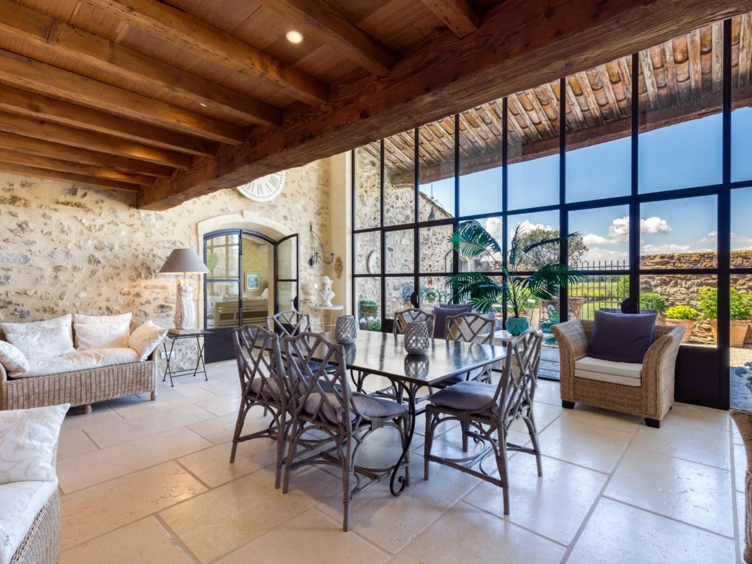 Farmhouse conservatory with dining table and armchairs under wooden beams with a large window overlooking a garden