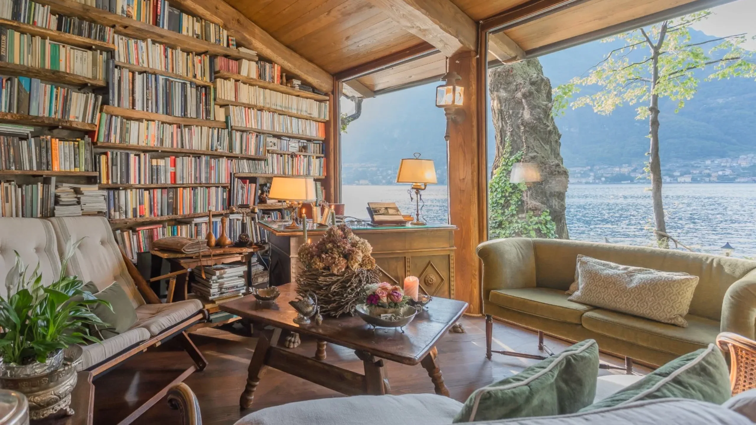 Living room with wall spanning bookcase, filled with a coffee table, chairs and looking out to a lake