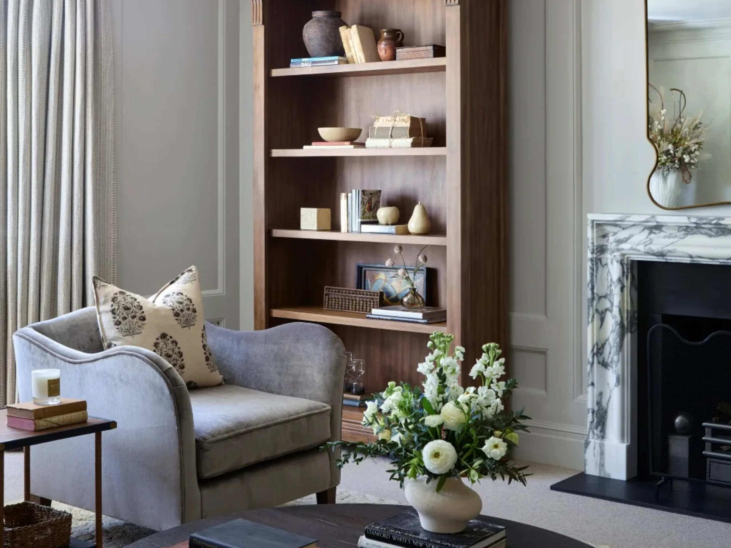 Living room with wooden bookcase, blue armchair, marble fire surround and flowers on a coffee table