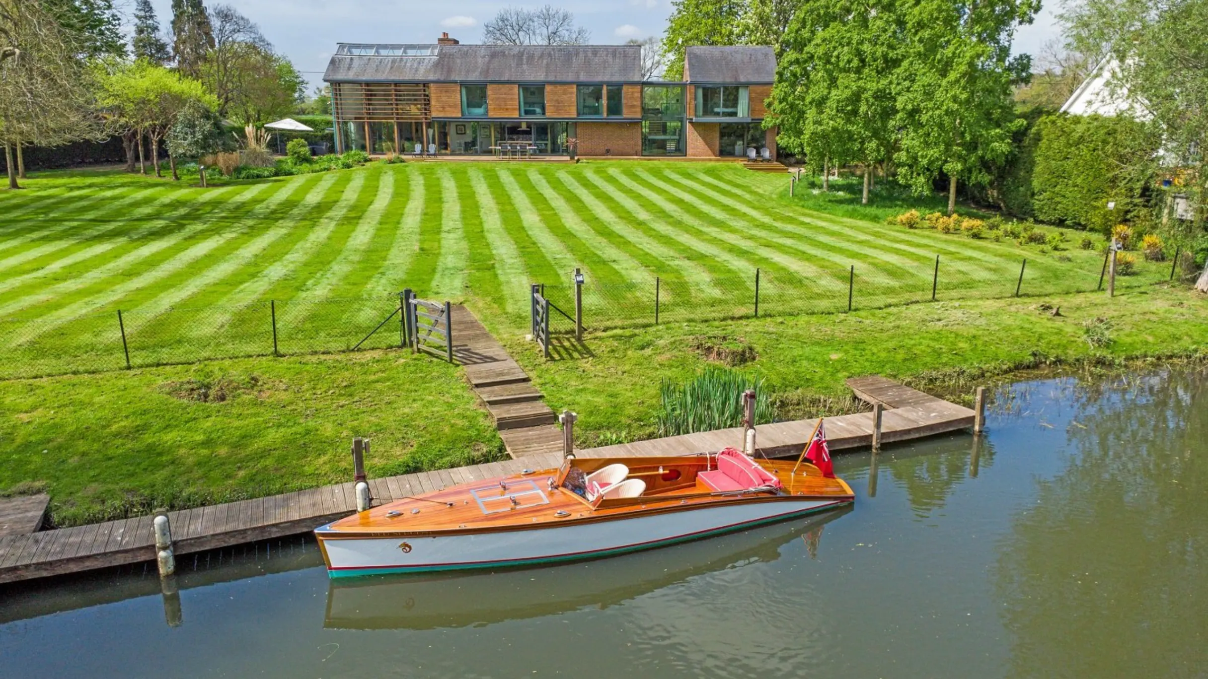 Exterior of a house and large lawn leading to a river with a boat