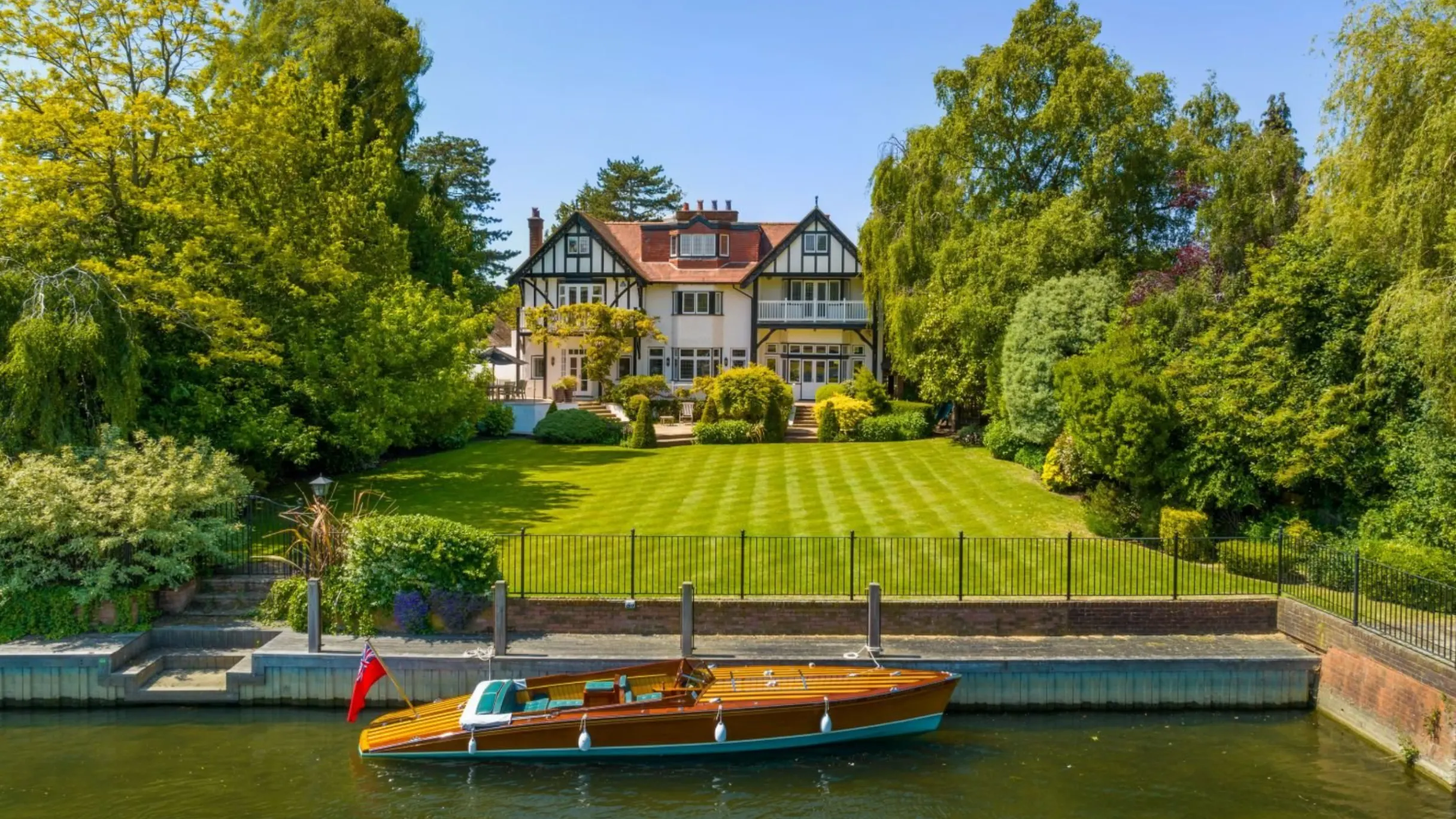 external view of period property with green garden in front and river with a boat in the foreground