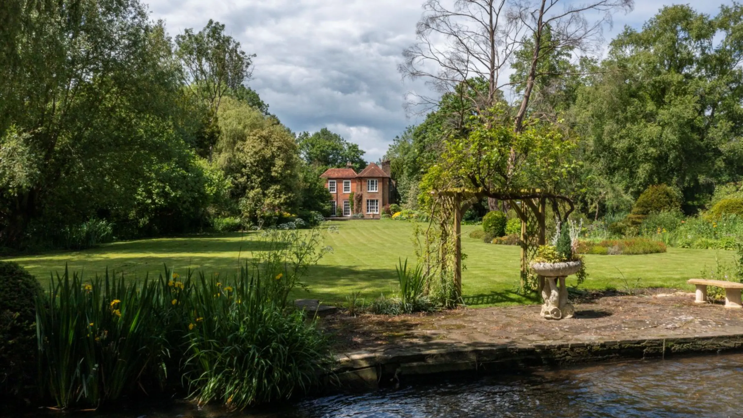 large garden with trees and a long lawn with the exterior of a house at the bottom