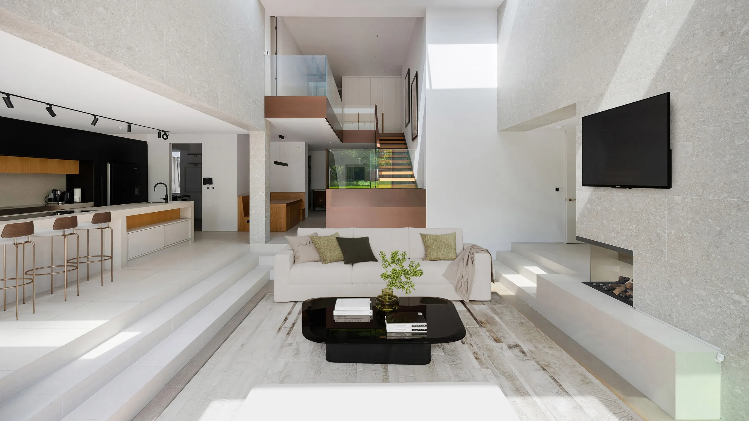 Modern living room with cream sofa, black coffee table, with a kitchen to the left and glass staircase in the background