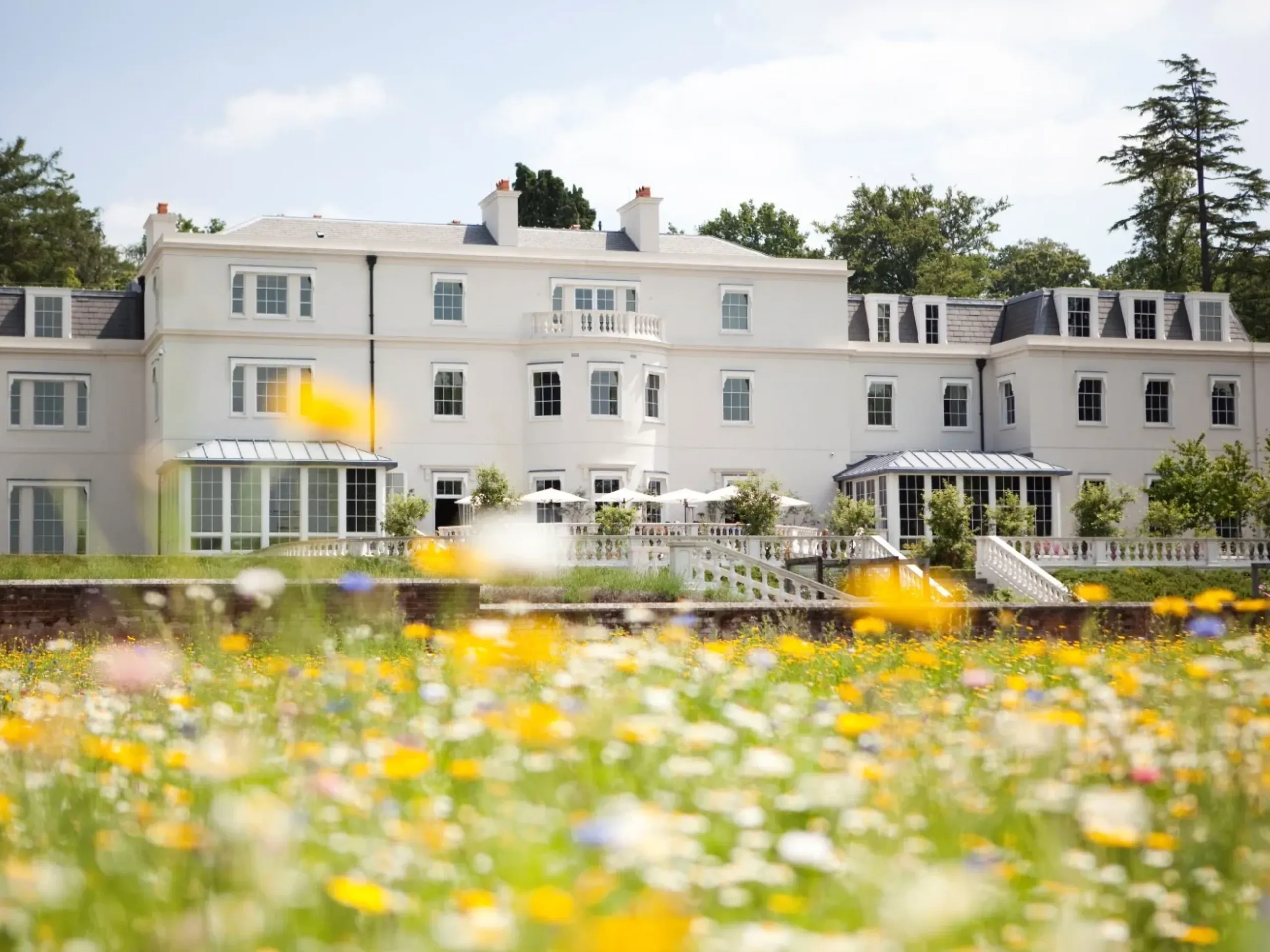 Exterior of Coworth Park hotel, a grand white building with a garden of wildflowers in front