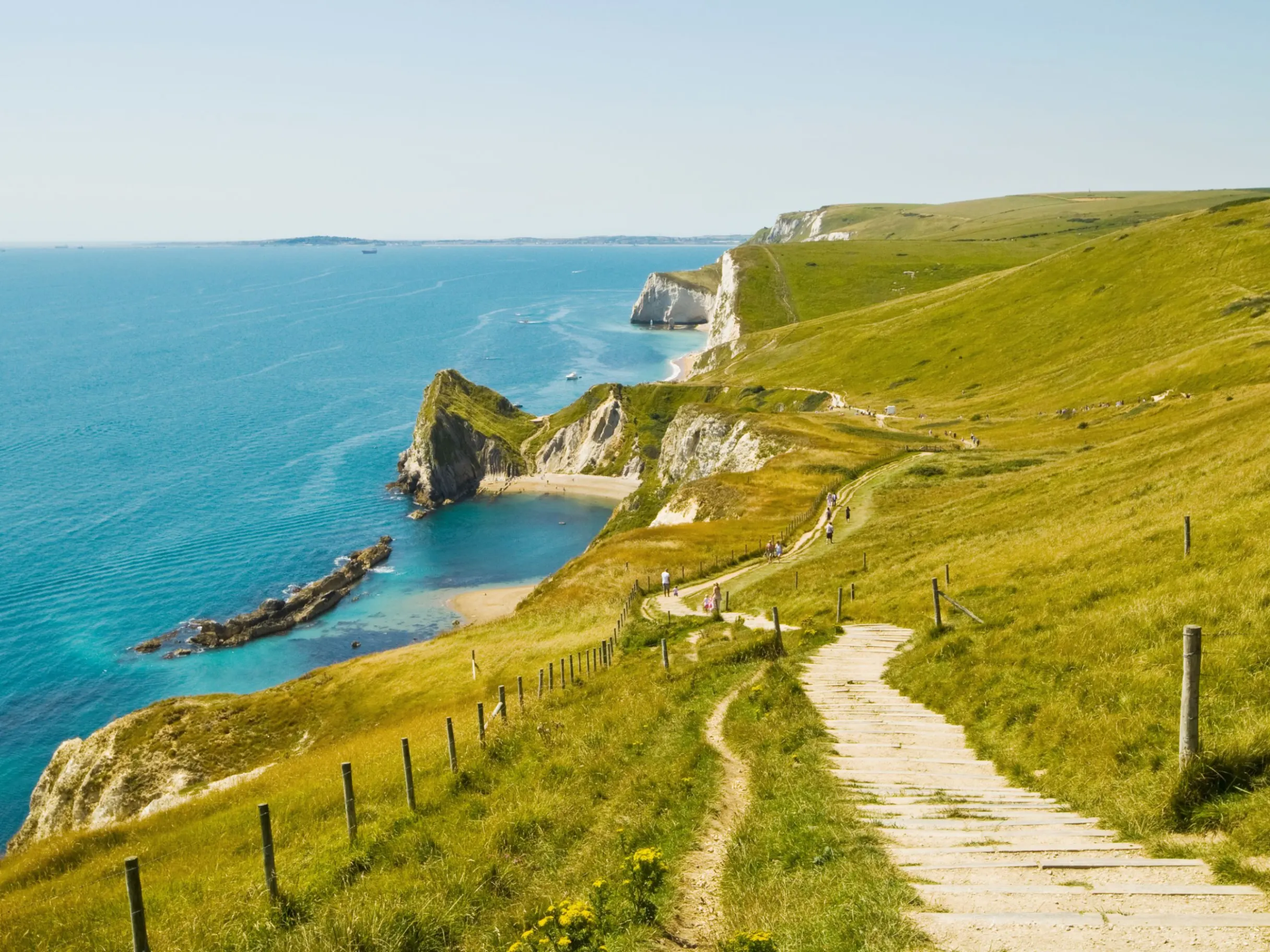 Coastline with green cliffs leading out to bright blue sea, under a clear blue sky