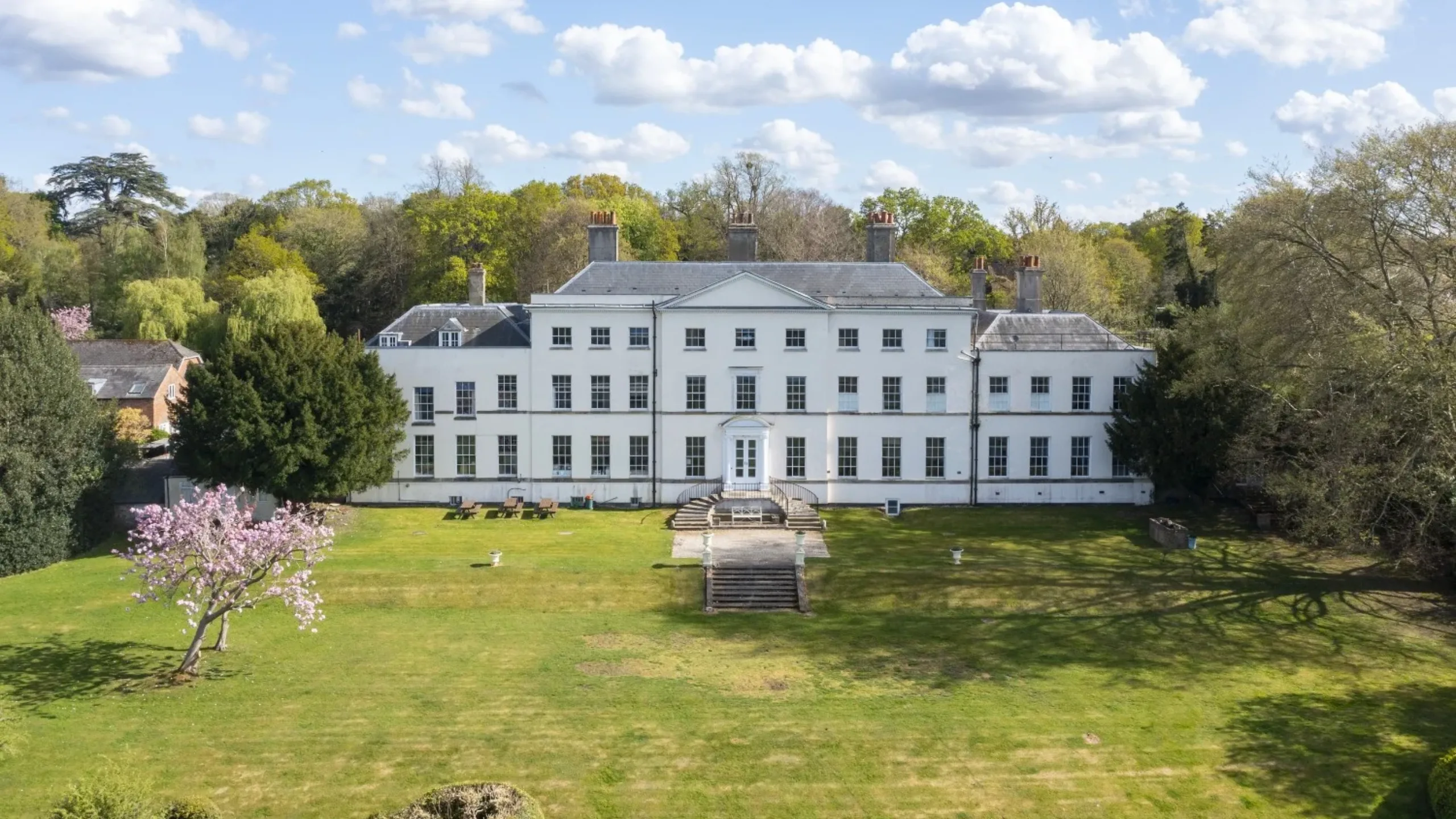 Large white mansion surrounded by a big green garden surrounded by trees