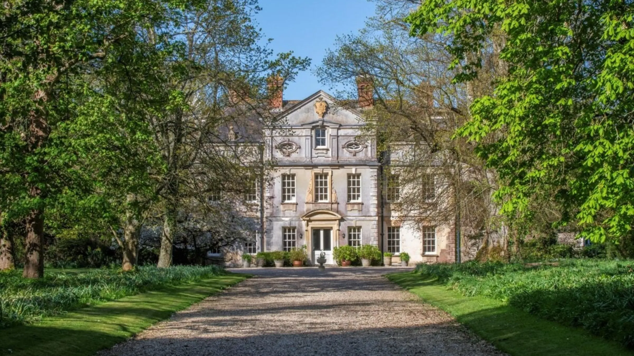 Exterior of a large period home with a long driveway leading up to it and trees on either side