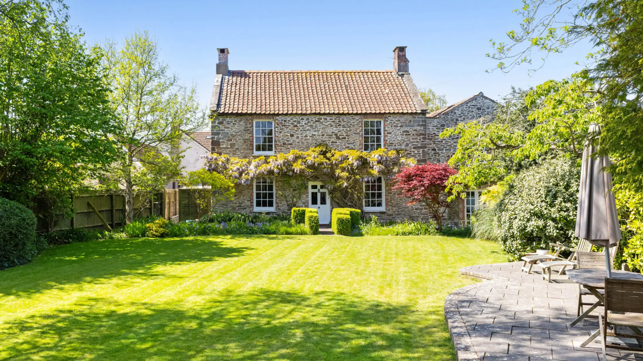 Exterior of a brick country house and rear garden with a green lawn flanked by green trees