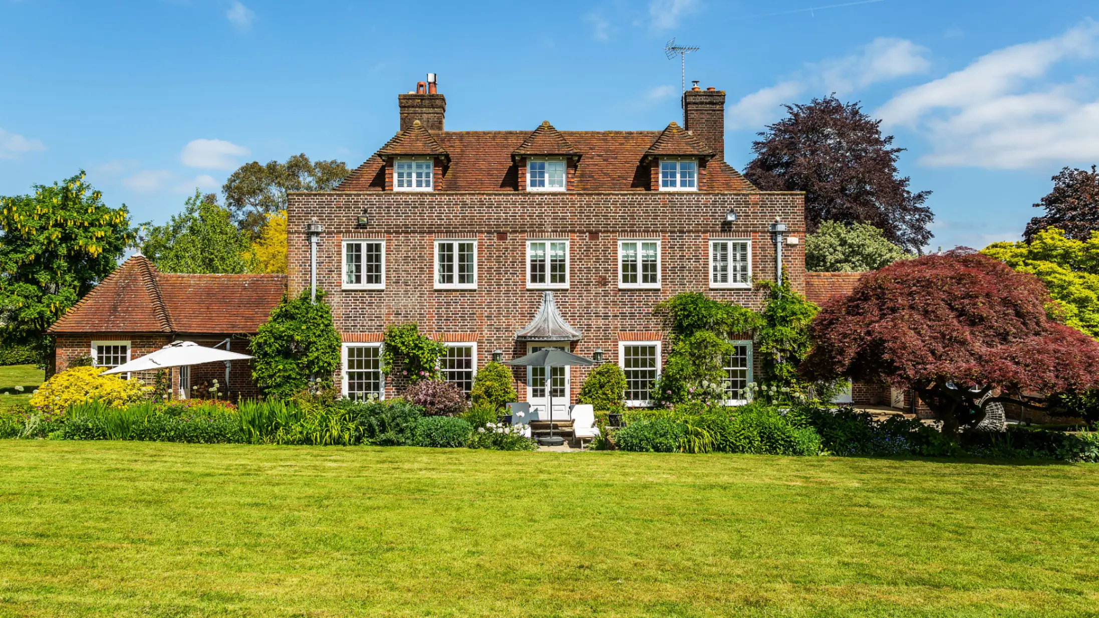 exterior-of-brick-country-house-surrounded-by-trees-and-a-green-front-garden