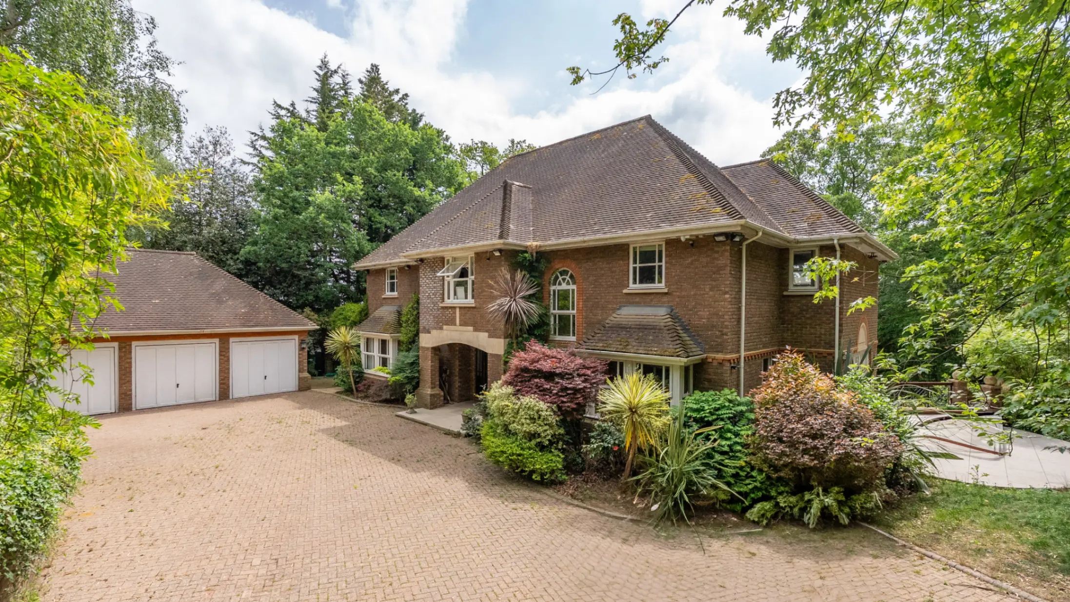 Exterior of detached brick house, with colourful bushes in front and a separate garage