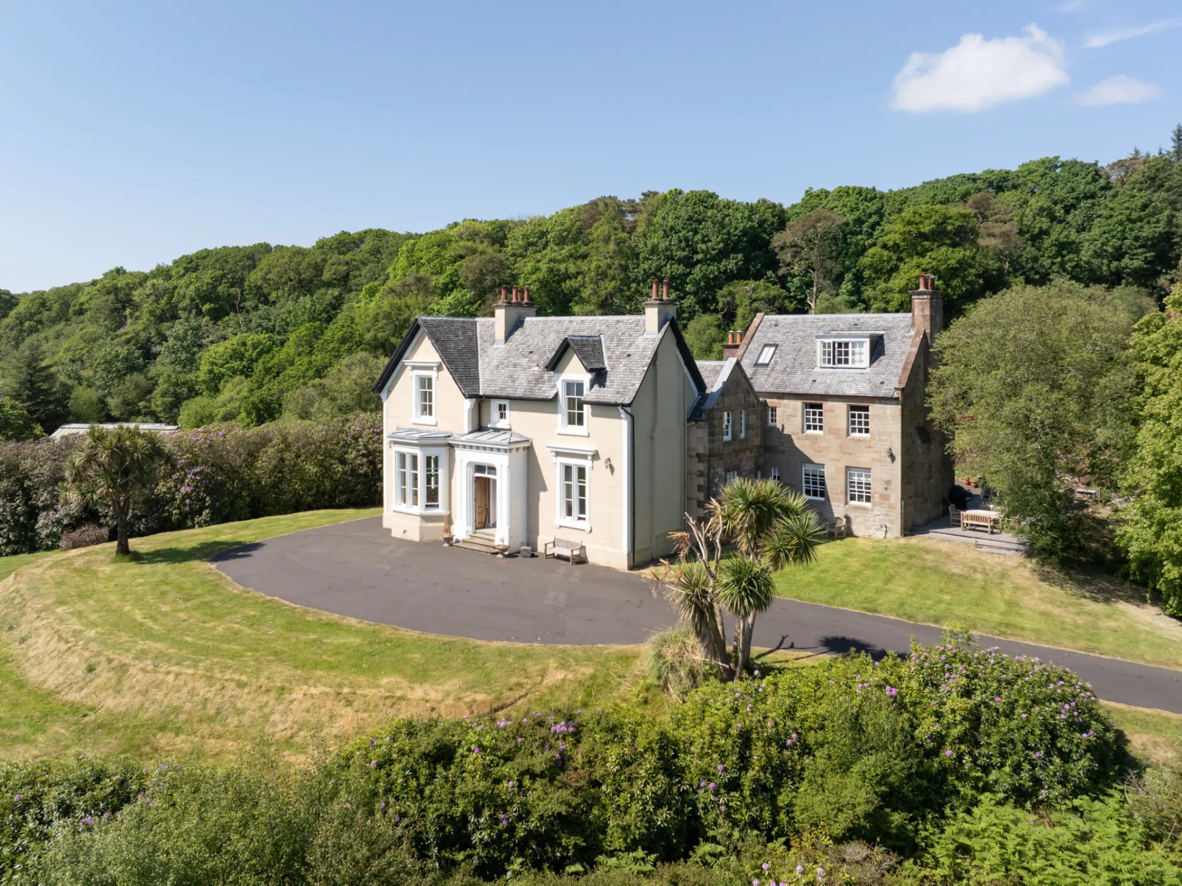 Exterior of large period home surrounded by mature green trees and a lawn in the foreground
