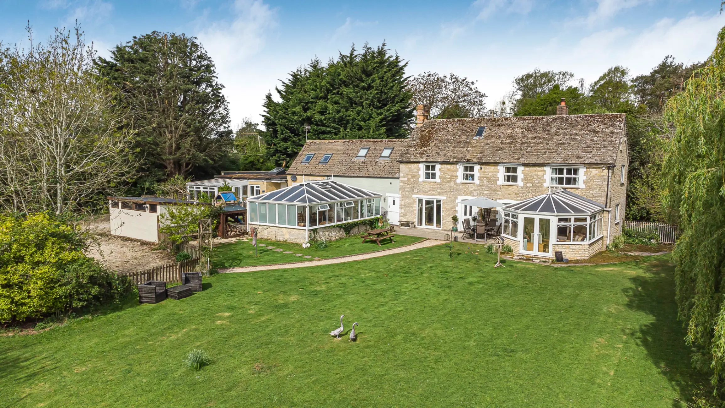 Exterior of brick country house with a conservatory and a glass outhouse, with a large green garden with mature trees