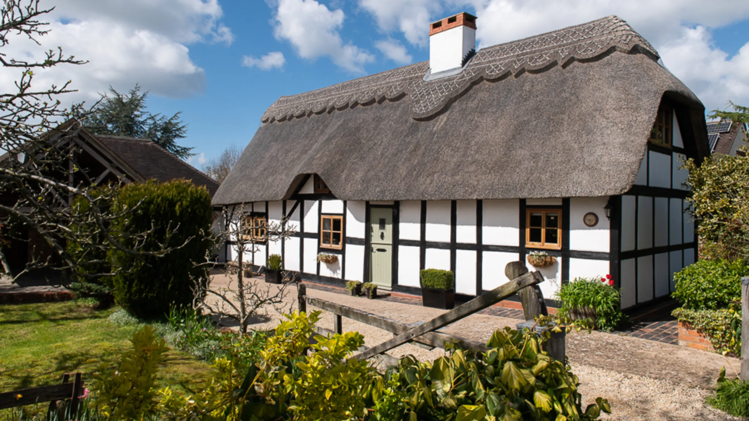 Exterior of a thatched cottage with a garden with bushes in front 