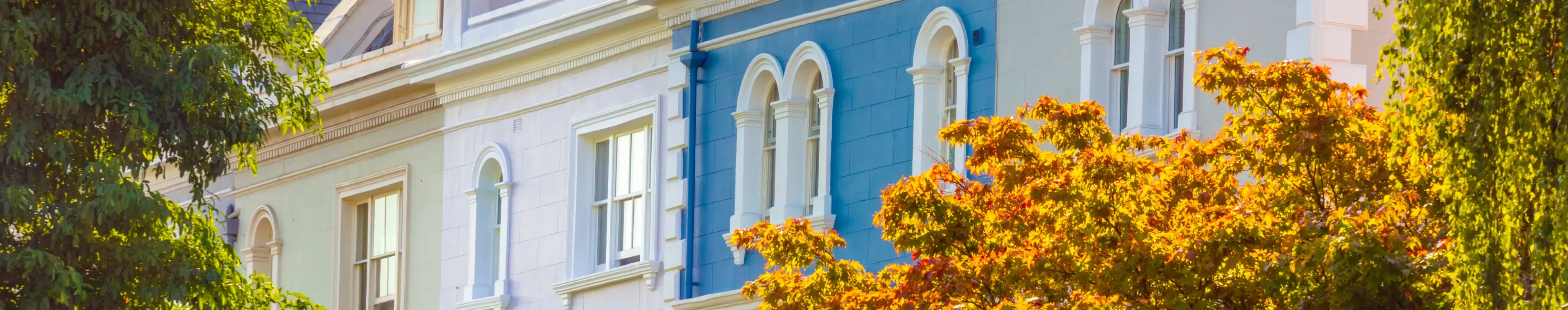 UK, London, Notting Hill. The facade of a luxurious traditional Regency style townhouses painted in bright colors and seen through Autumn trees