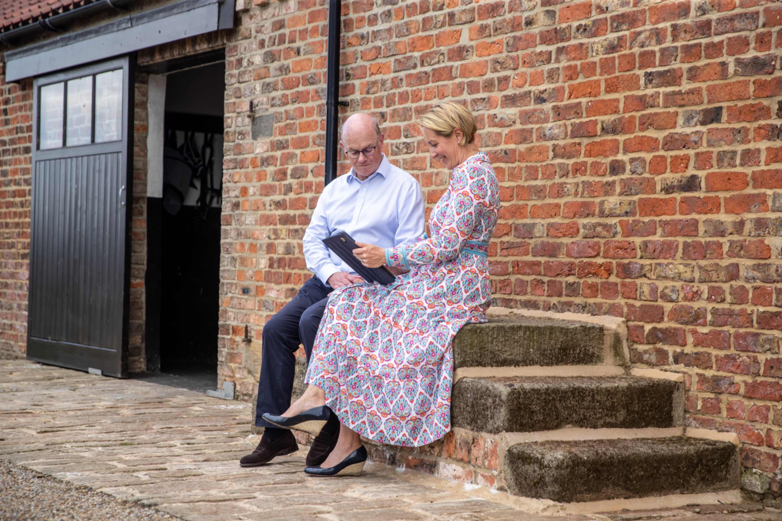 A woman and man sitting on steps outside a rural property