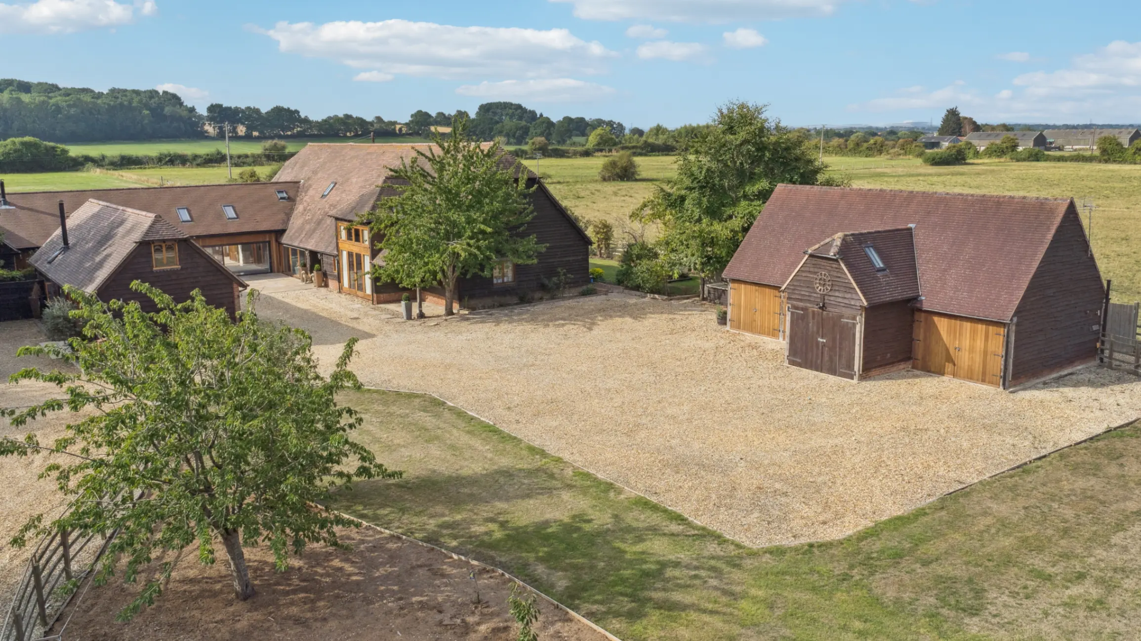 Exterior of country home and a separate cottage set amongst a large green field with mature trees 