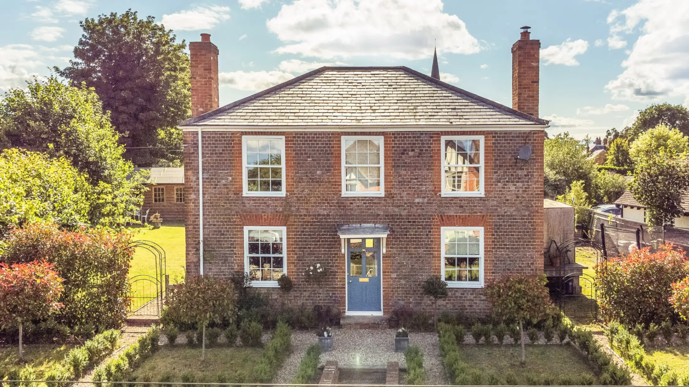 Exterior of a brick country house surrounded by bushes and mature trees