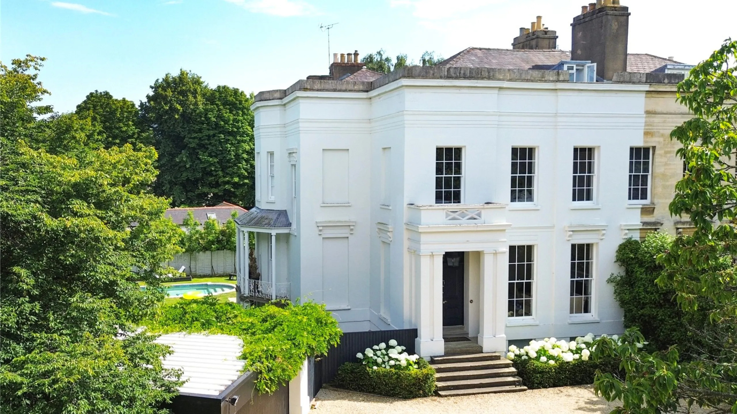 Exterior of white grade II listed Regency Villa with a swimming pool in the background and mature trees to the side