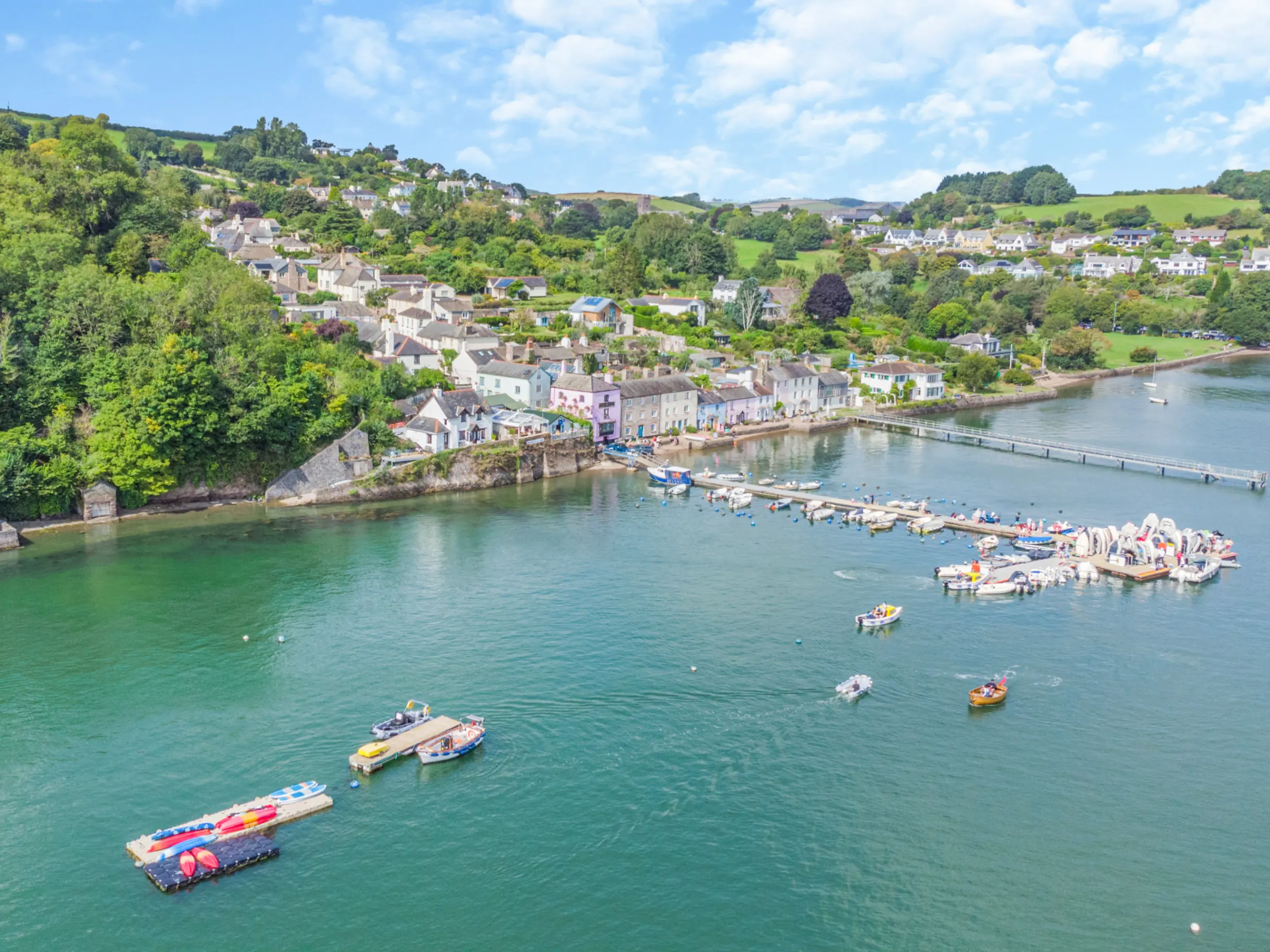 Ariel view of Devon houses next to the River Dart with boats and an elevated boardwalk 