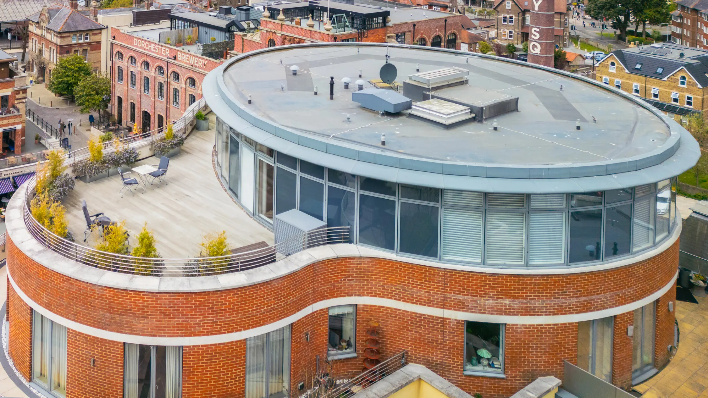 Rounded red brick modern building, with a rooftop deck with a brewery, buildings and houses in the background