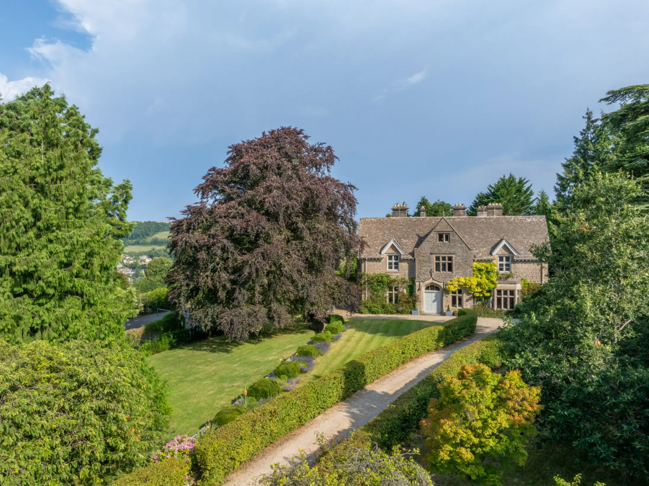 Exterior of a large country period home surrounded by mature trees and a large garden
